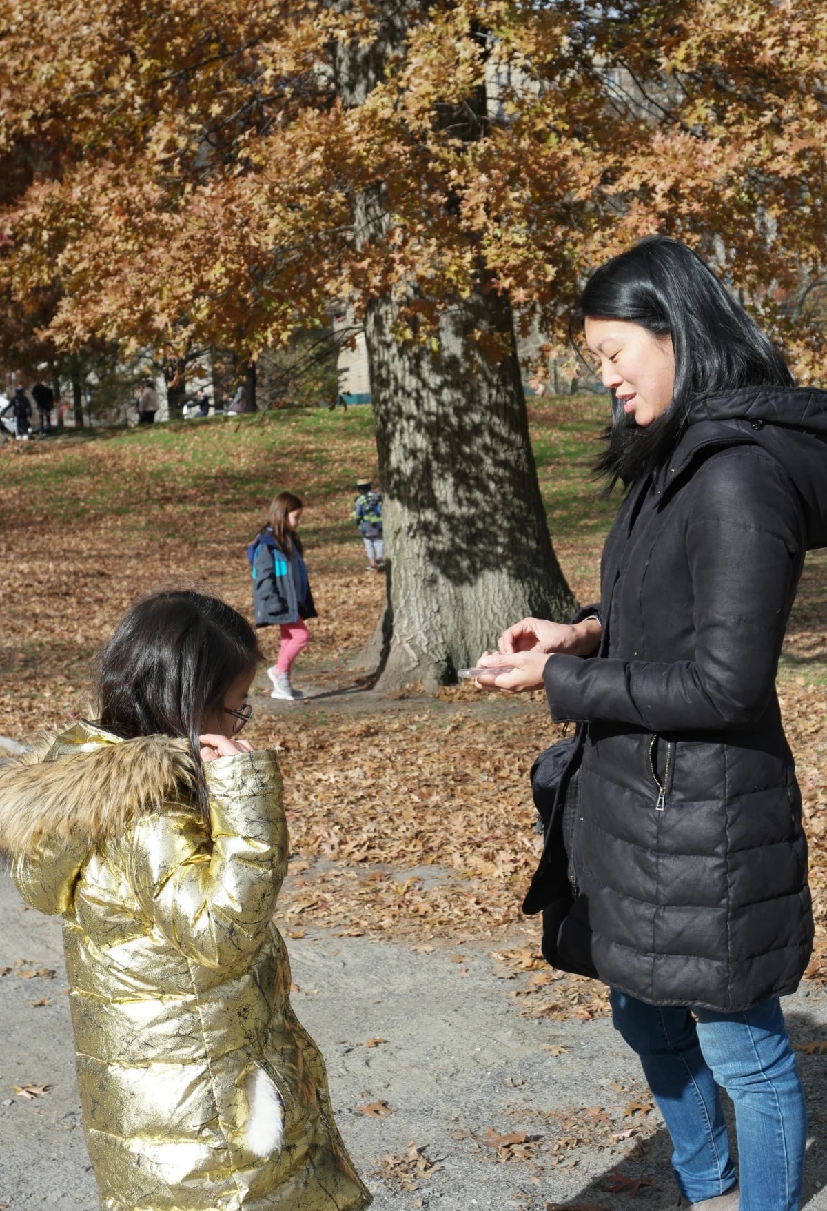 A lower school student in a shiny gold coat talks to a teacher with Central Park behind them