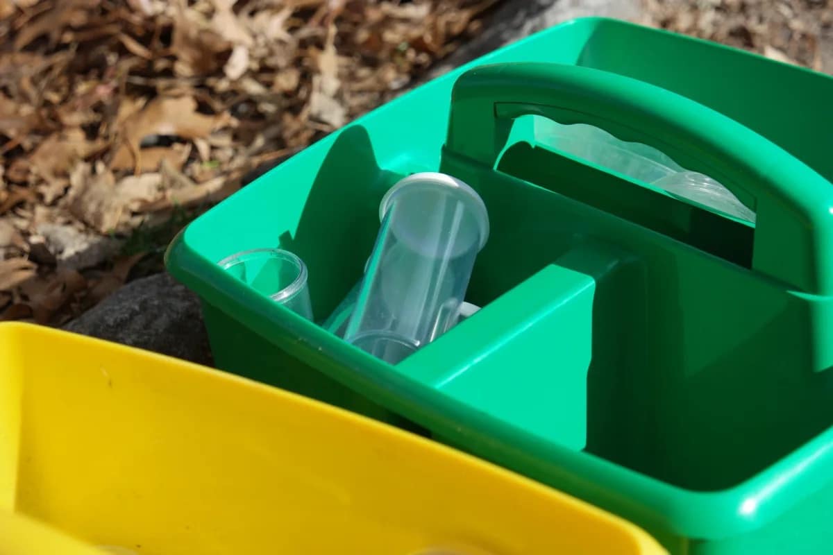 Beakers are shown in a green carrying case, set on the ground atop autumnal leaves