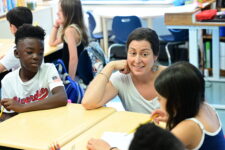 Fieldston Lower teacher guides student with a smile in the classroom.