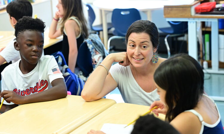 Fieldston Lower teacher guides student with a smile in the classroom.