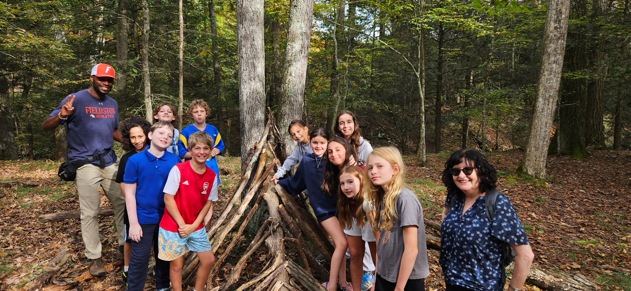 Ethical Culture students and teachers pose in front of wooden shelter on Ashokan outdoor learning trip.