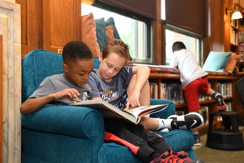 Students read book together while sitting on chair in library