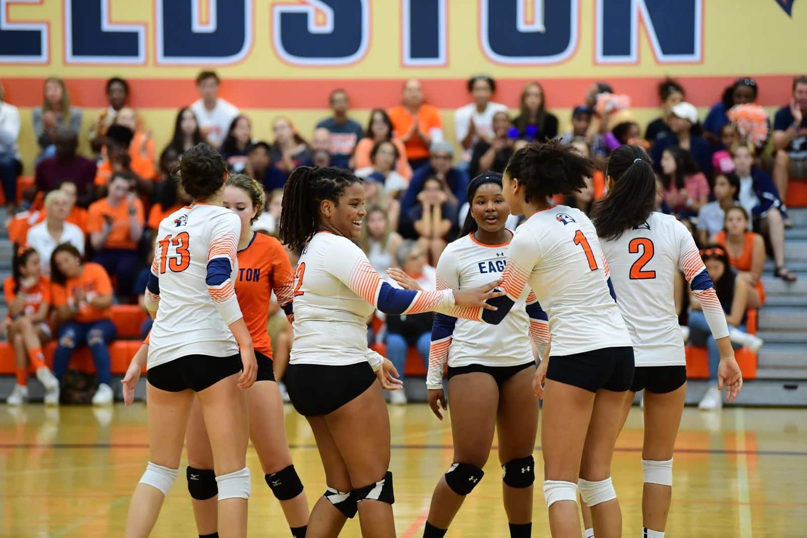 Girls varsity volleyball players cheer in celebration on court