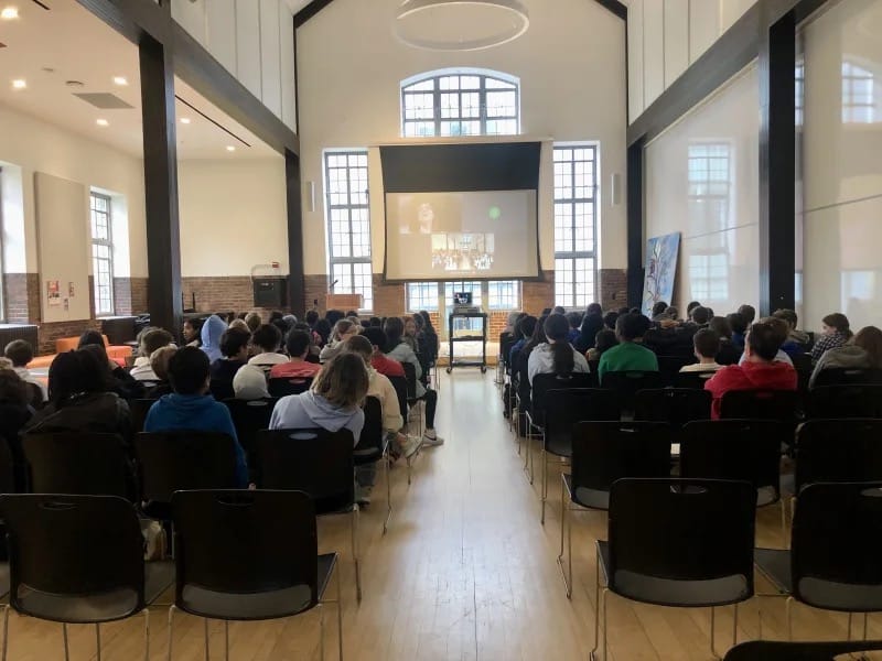 Students sit in Student Commons and watch speaker on big screen