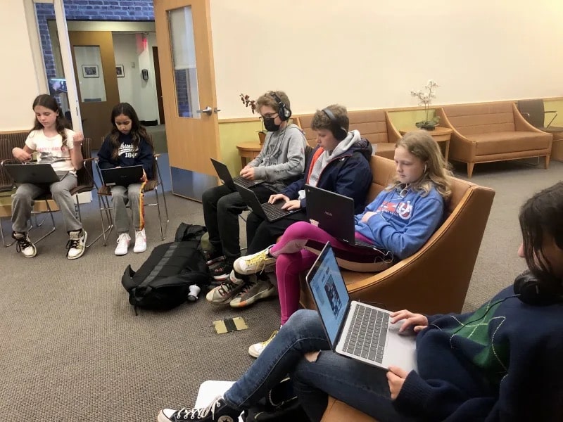 Students sit in circle with computers and engage in discussion