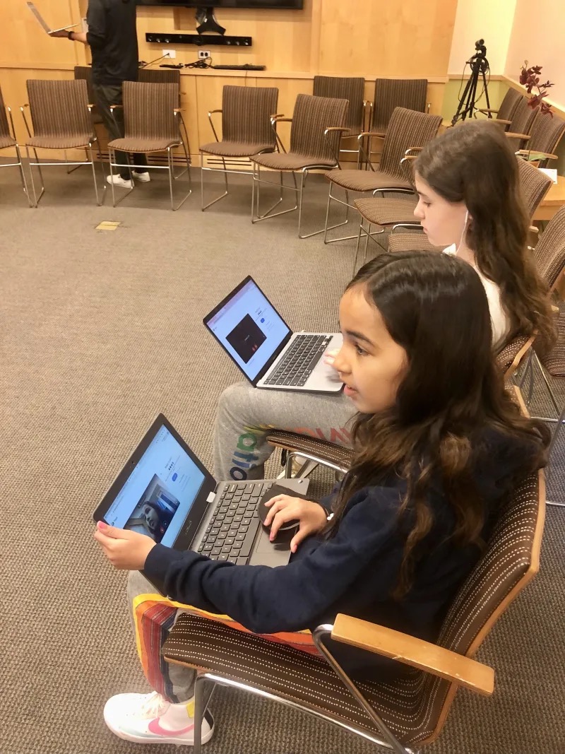 Two students sit with computers and engage in discussion
