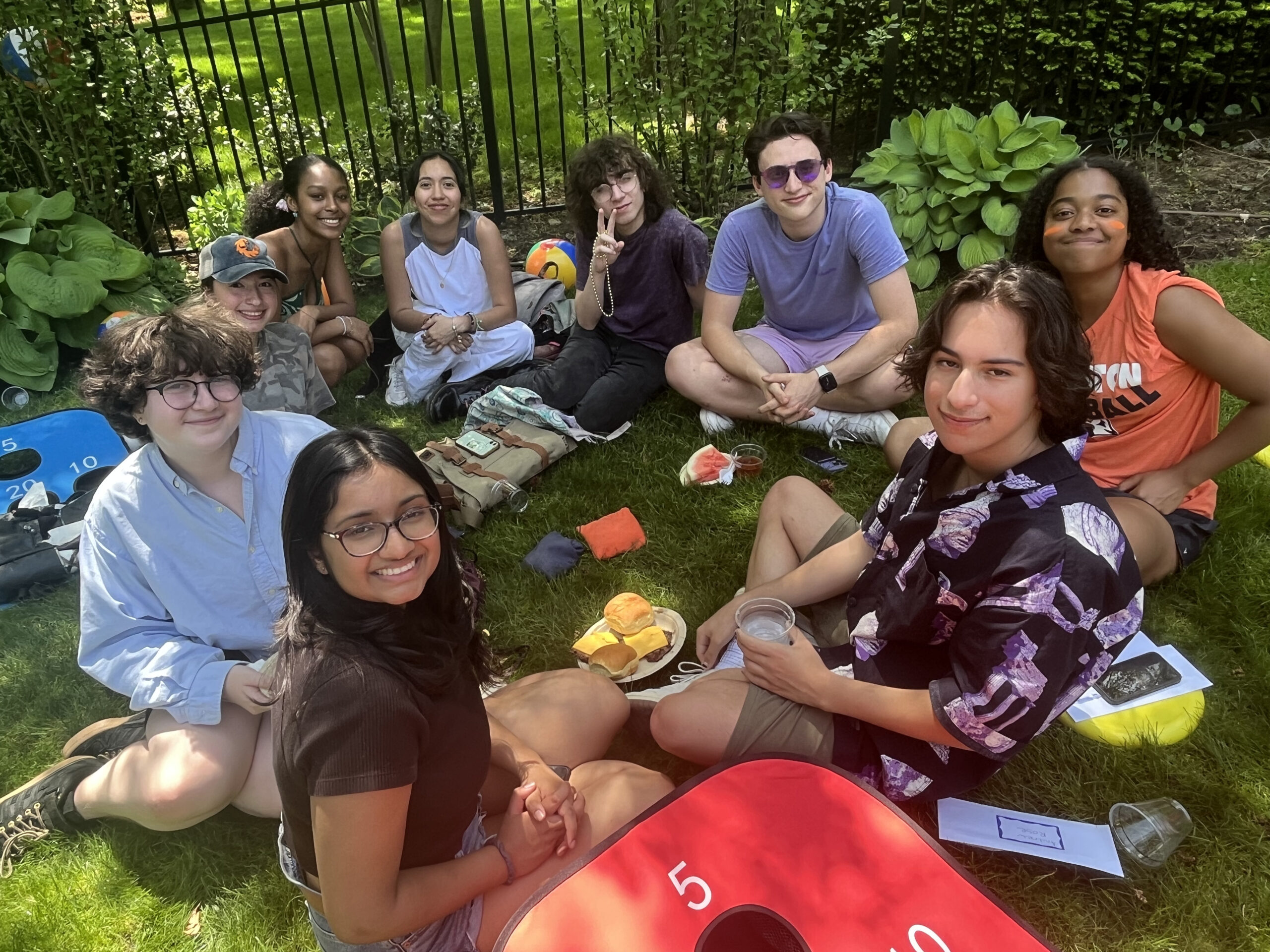 A group of students smile at the camera while sitting in the grass at the senior barbecue