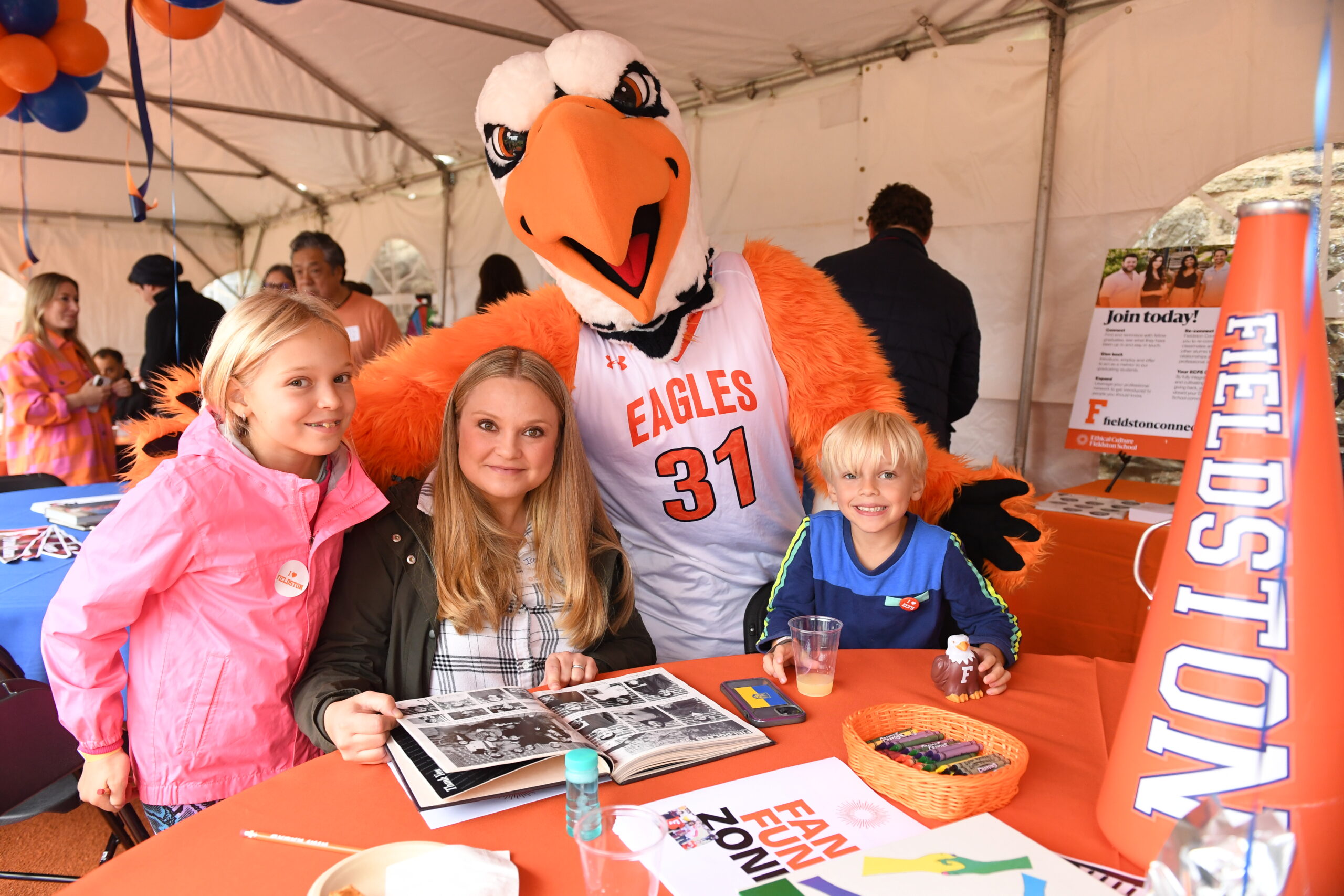 The Eagle poses in the alumni tent with one alumni and two students