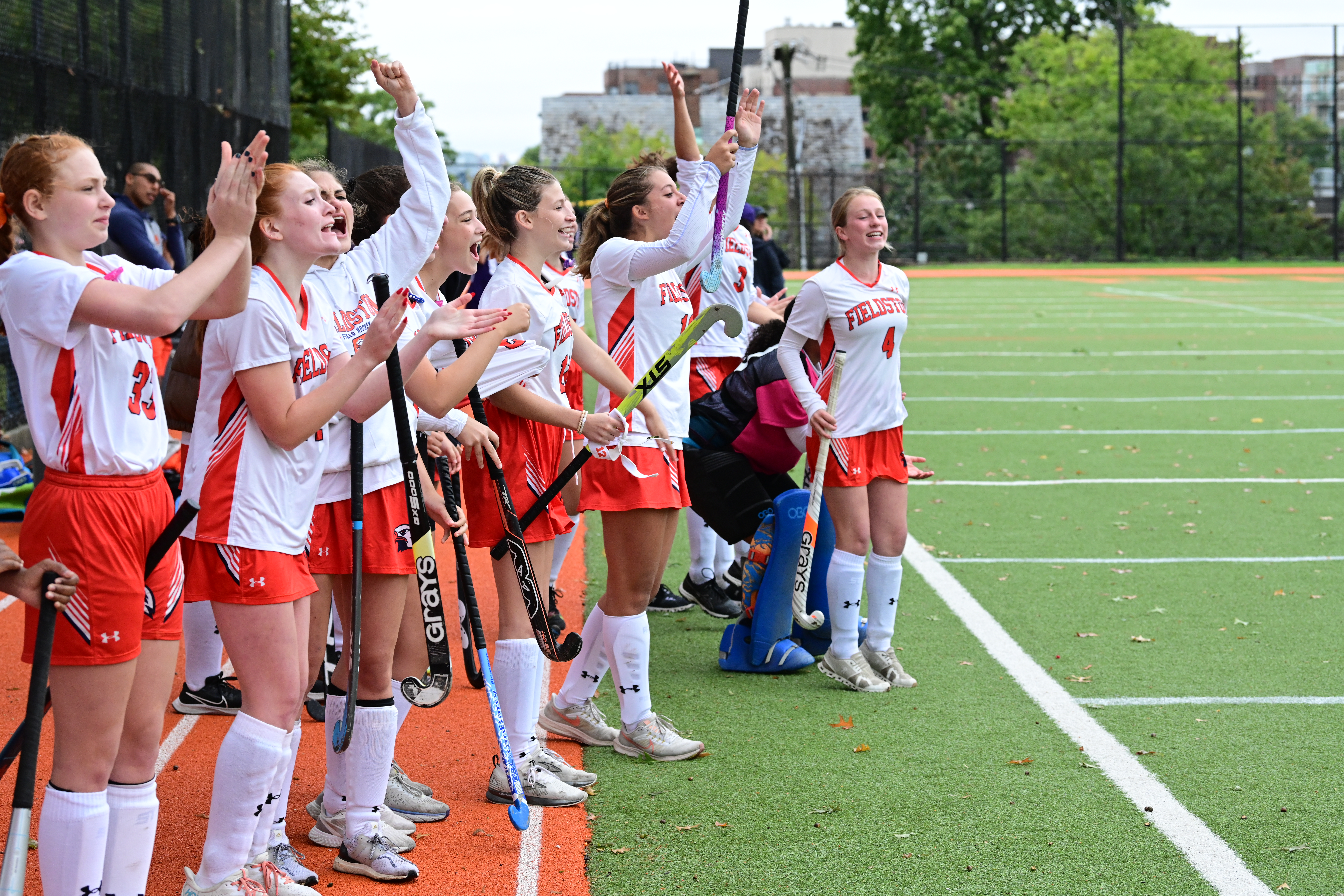Field hockey players celebrate on the sidelines as their teammate scores a point