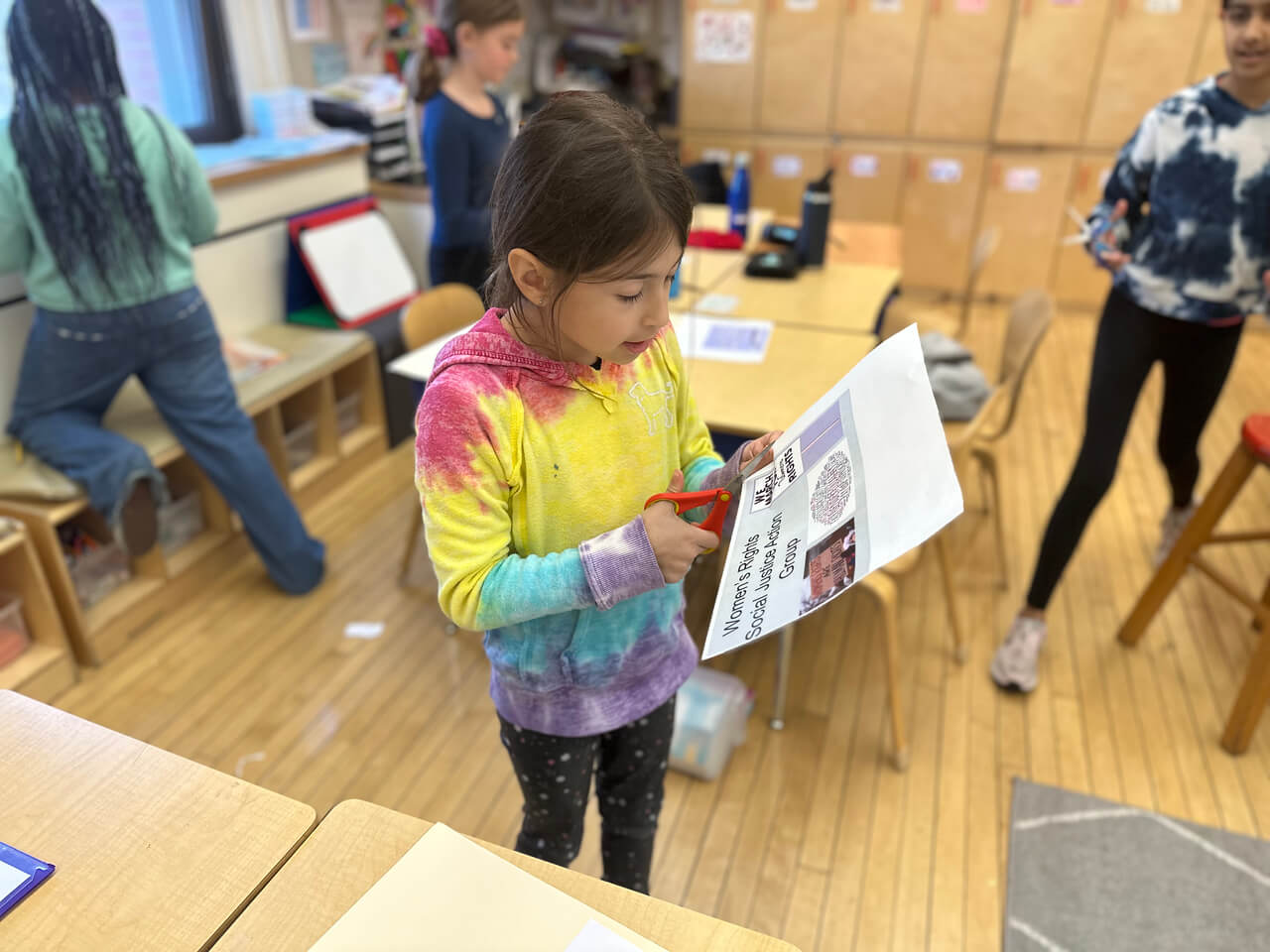 Ethical Culture Student uses scissors to cut out a title page for her women's rights poster.