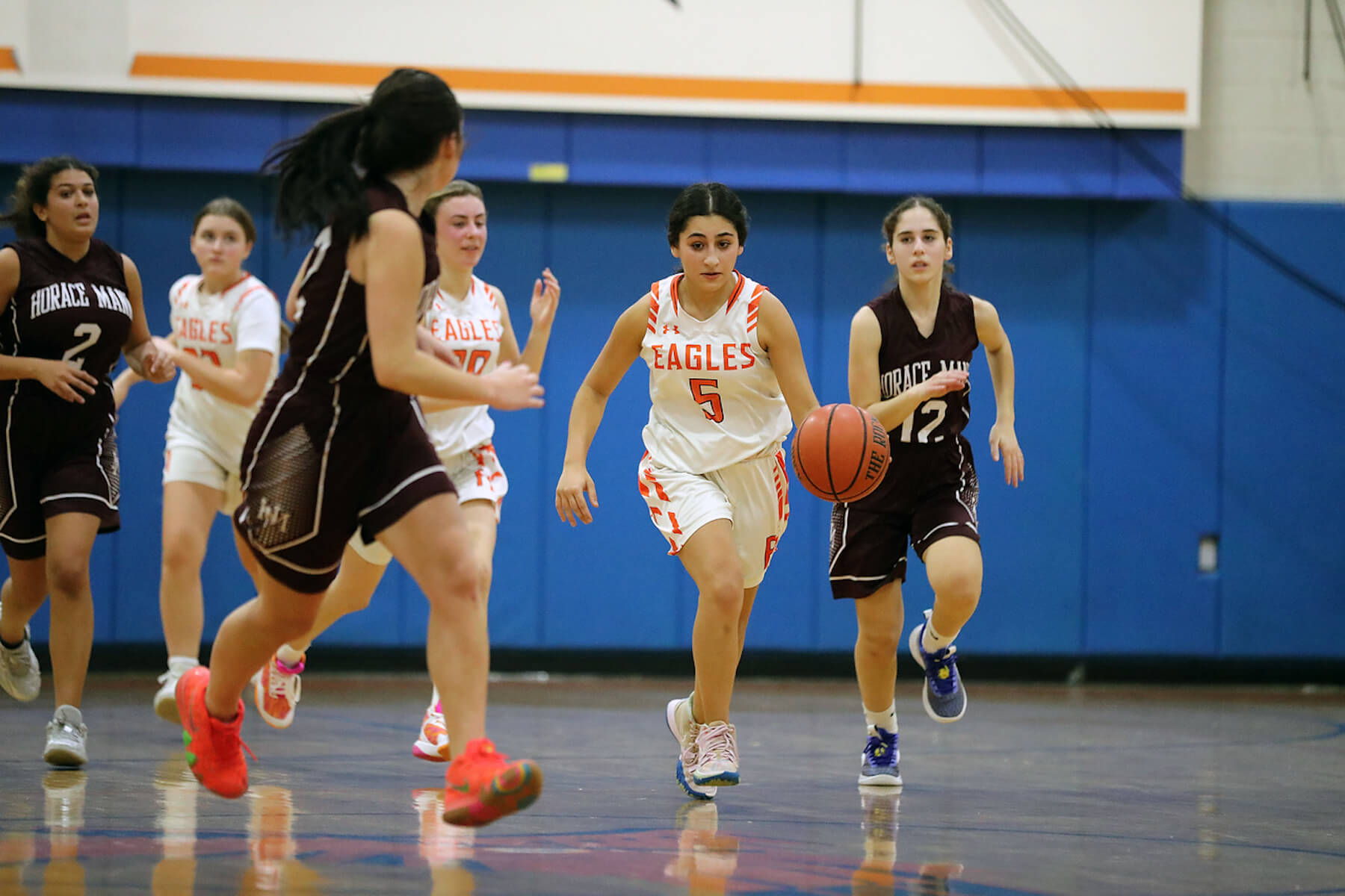 Fieldston Upper girls basketball player dribbles the ball up the court, surrounded by teammates and members of the opposing team.