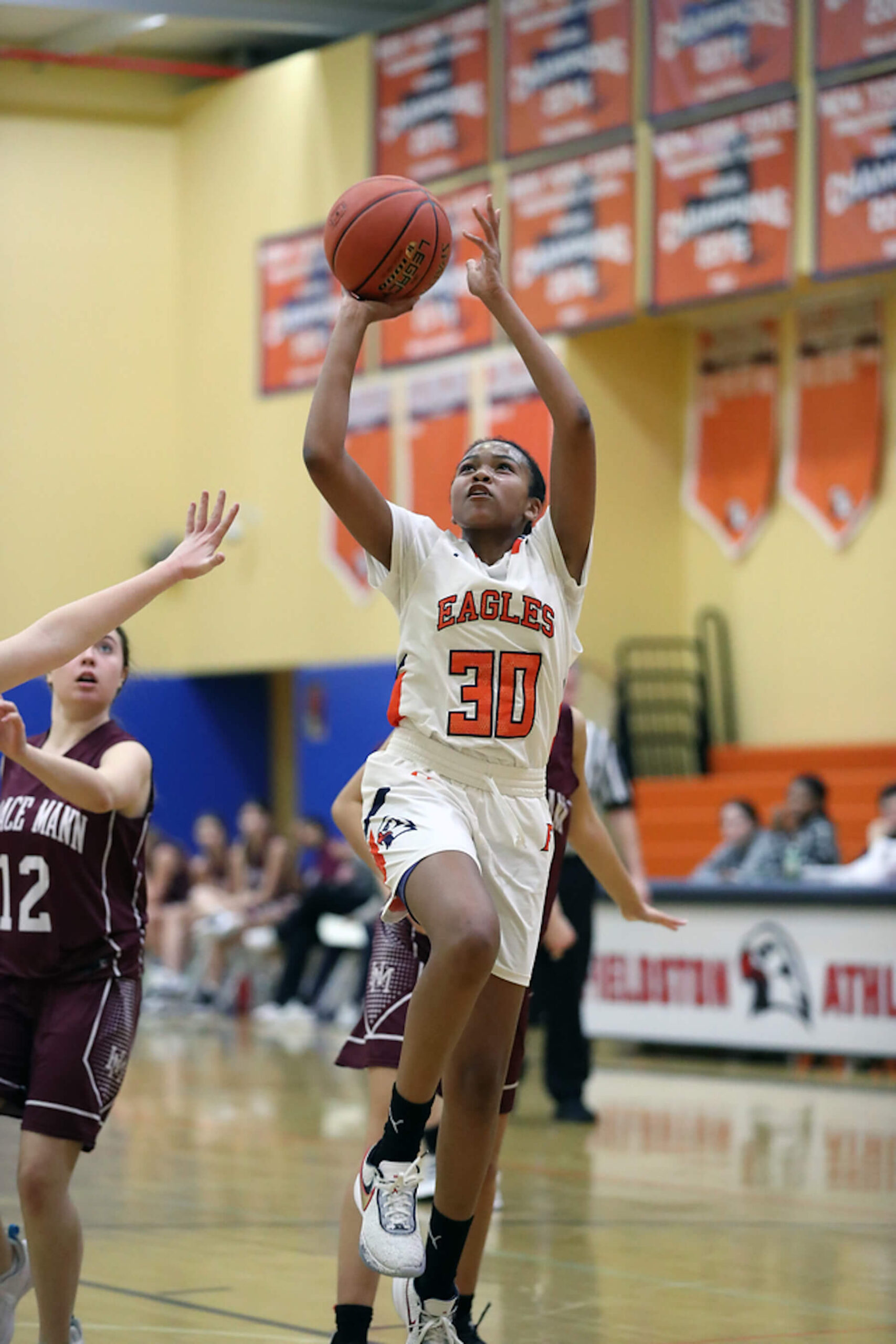 Fieldston Upper girls varsity basketball player goes up for a layup as two players on the opposing team follow close behind.