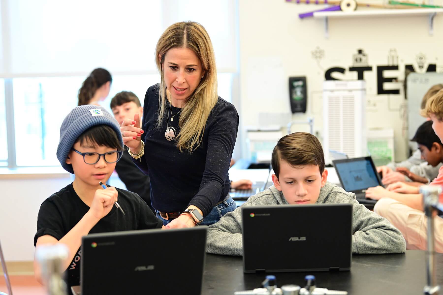 Ethical Culture Fieldston School Middle School students looking at computer with Teacher looking over shoulder to help