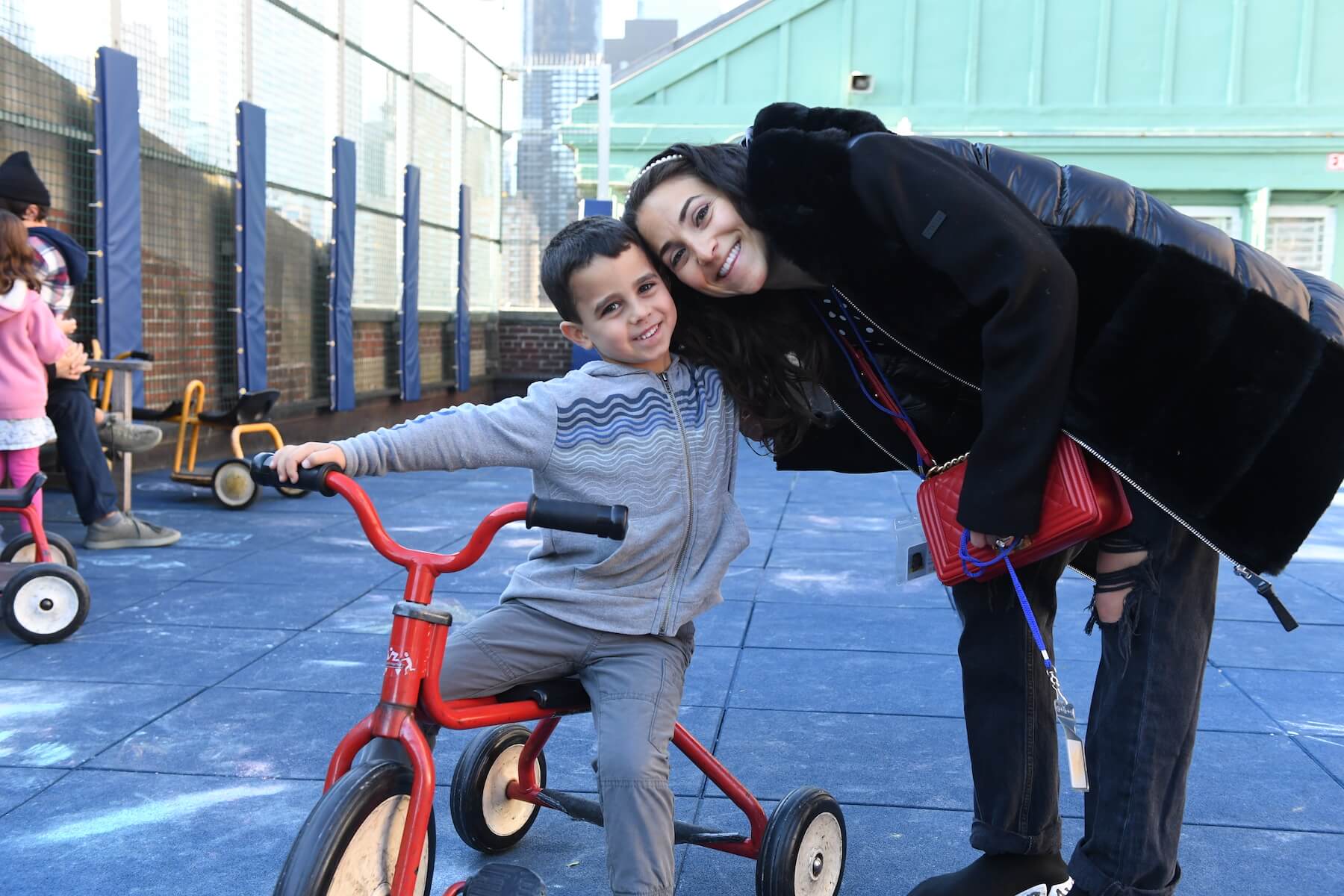 Ethical Culture Fieldston School student riding a tricycle on Ethical Culture playground smiling with a teacher