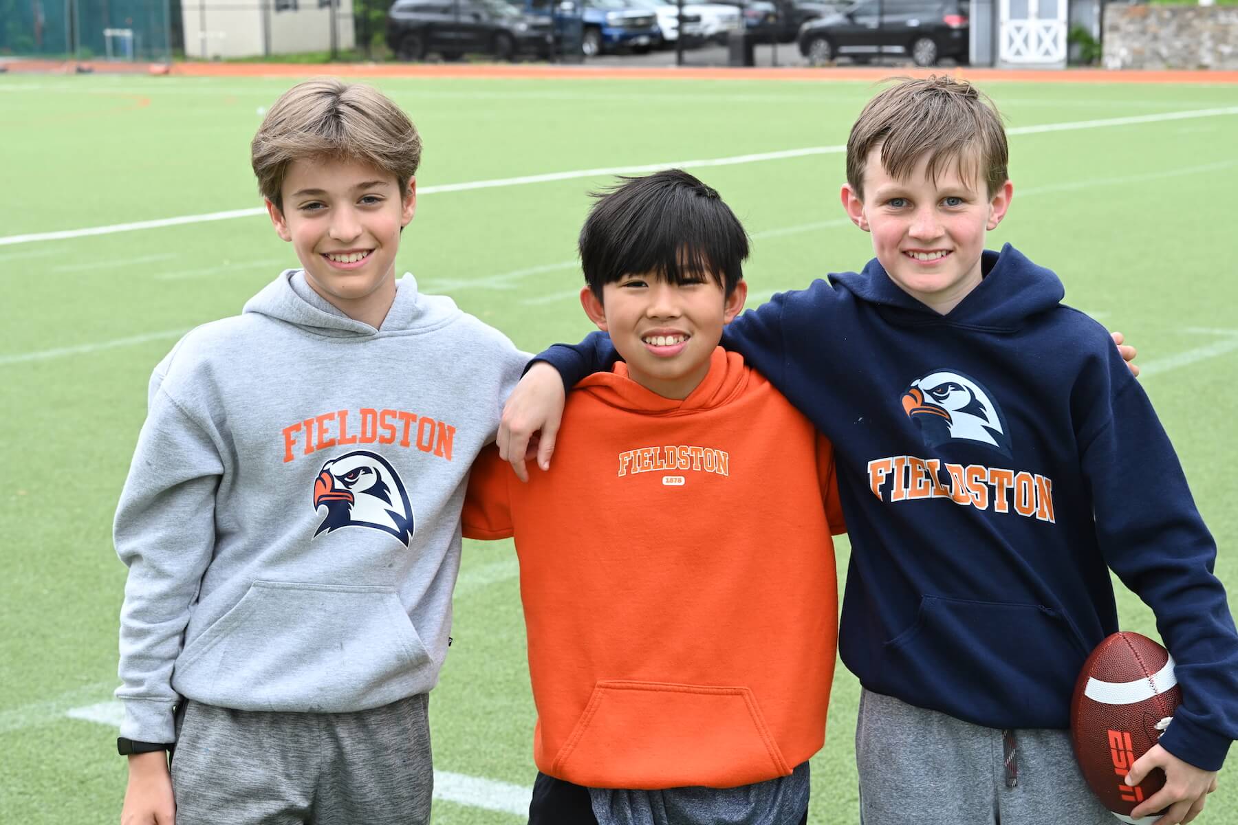 Ethical Culture Fieldston School three Middle School students pose for a group shot on the field in their Fieldston gear