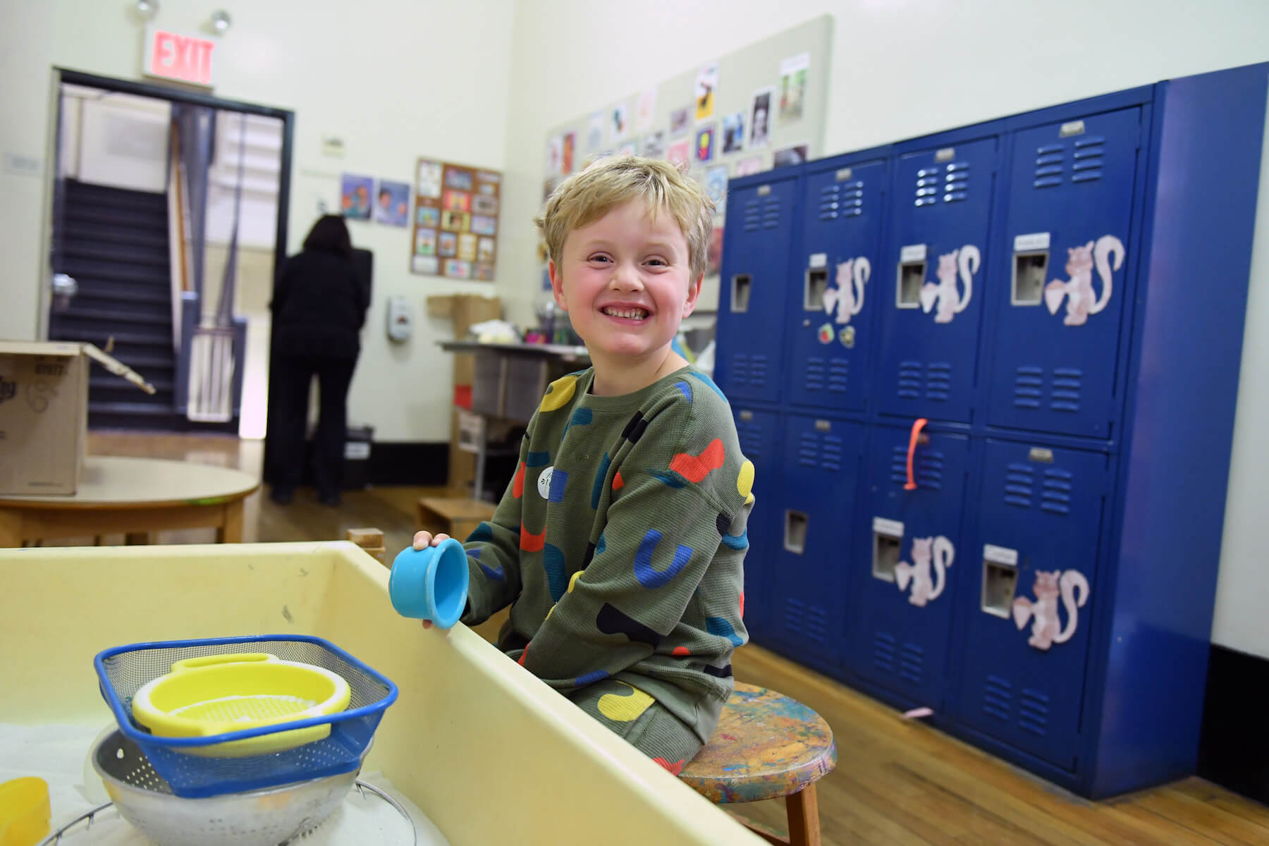 Ethical Culture Fieldston School Ethical Culture student smiles at the camera while playing with the sand table