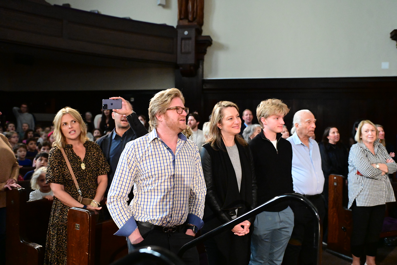 Family of Lucy Simon Levine ’58 stands in the audience and sings along to the Ethical Culture school song.