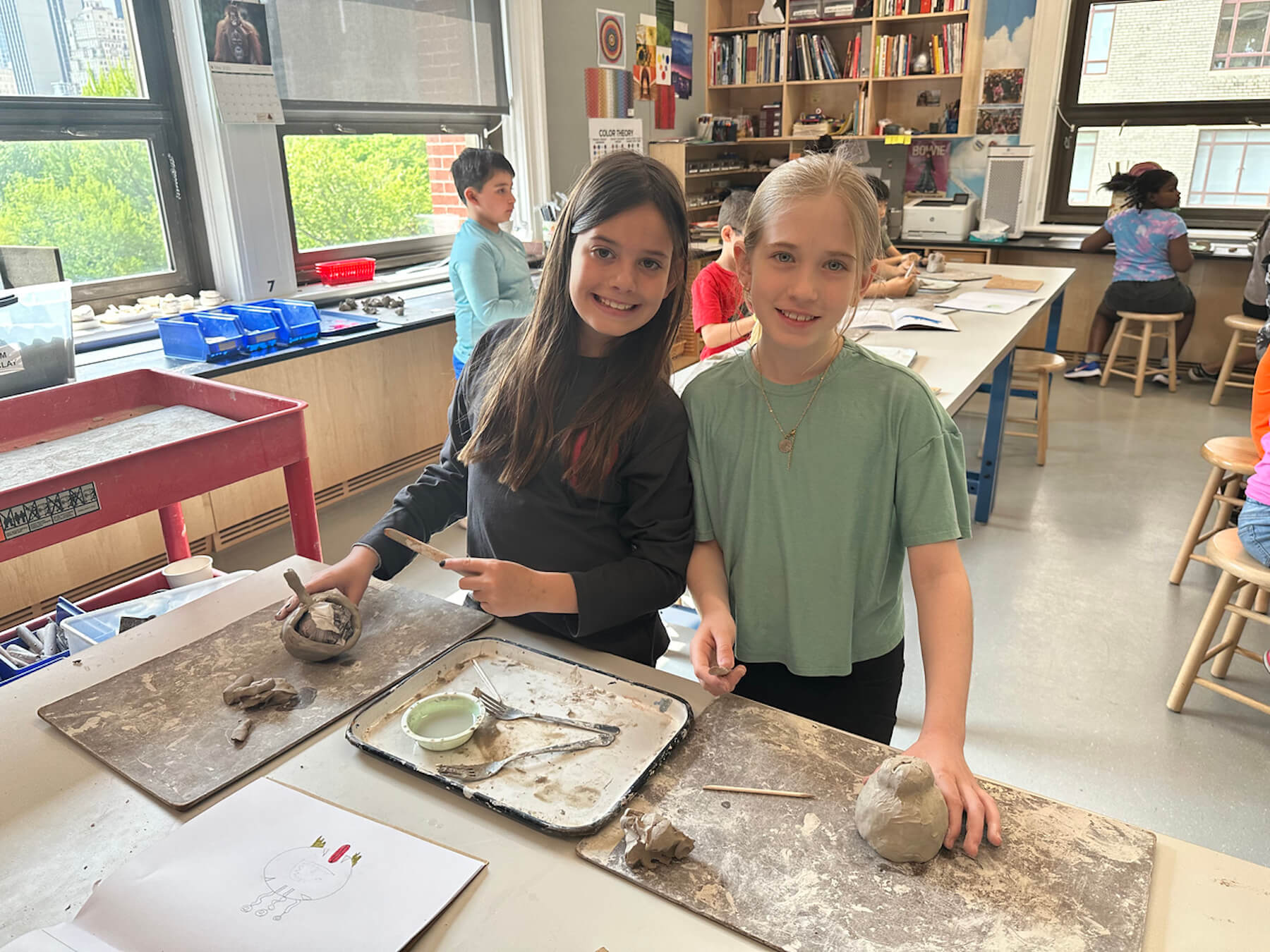 Ethical Culture 2nd Grade students pose and smile with their ceramics projects in art classroom.