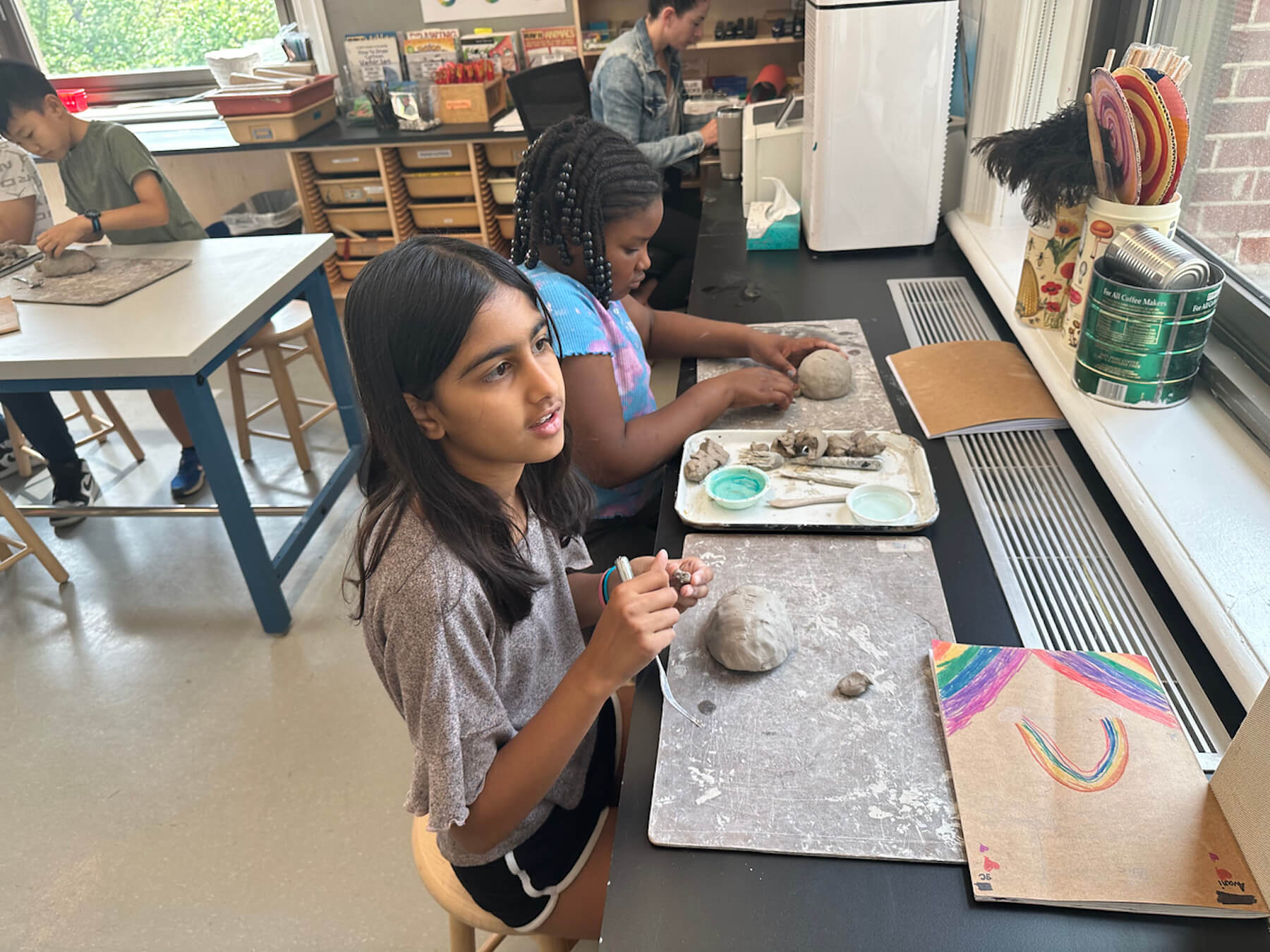 Ethical Culture students sit in front of window in art room working on their ceramics projects.