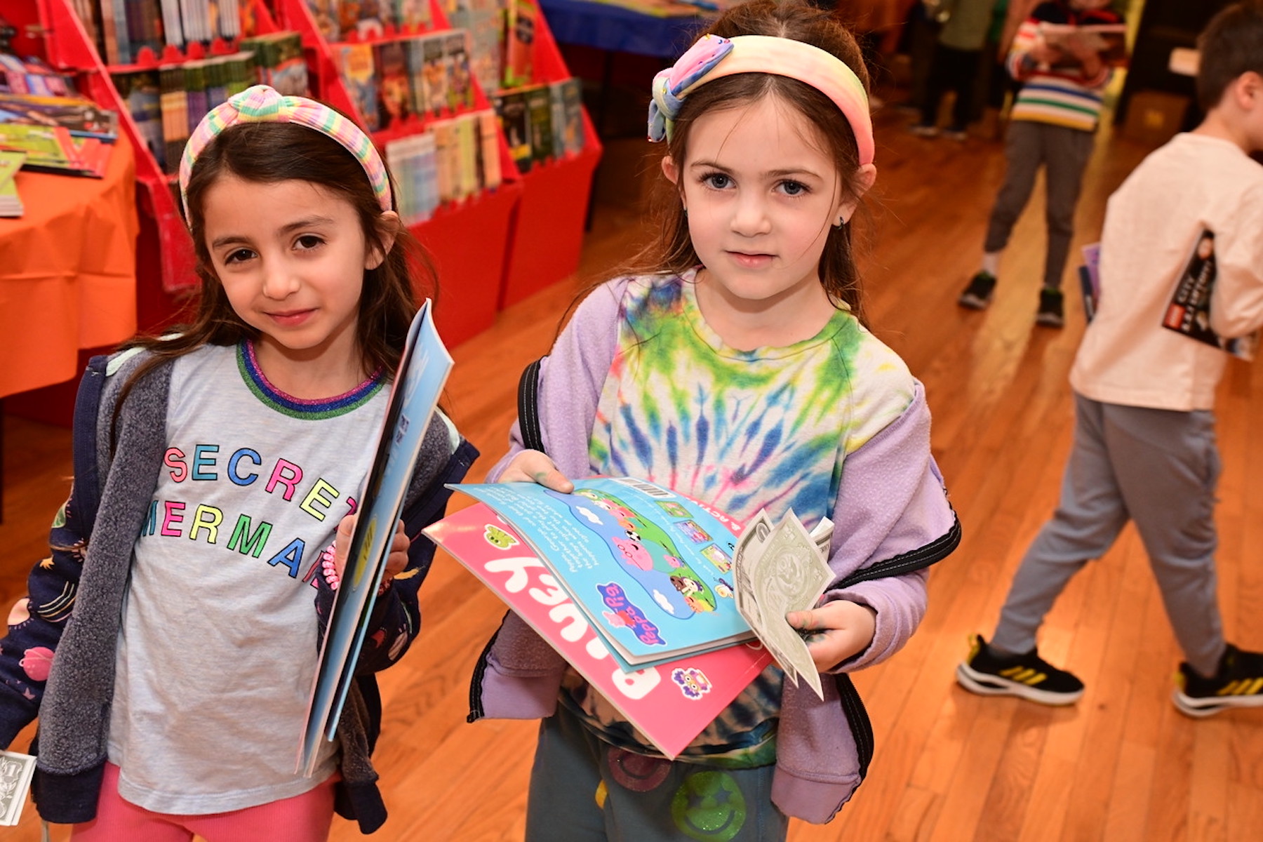 Two students smile and hold up their books at the Ethical Culture Book Fair.