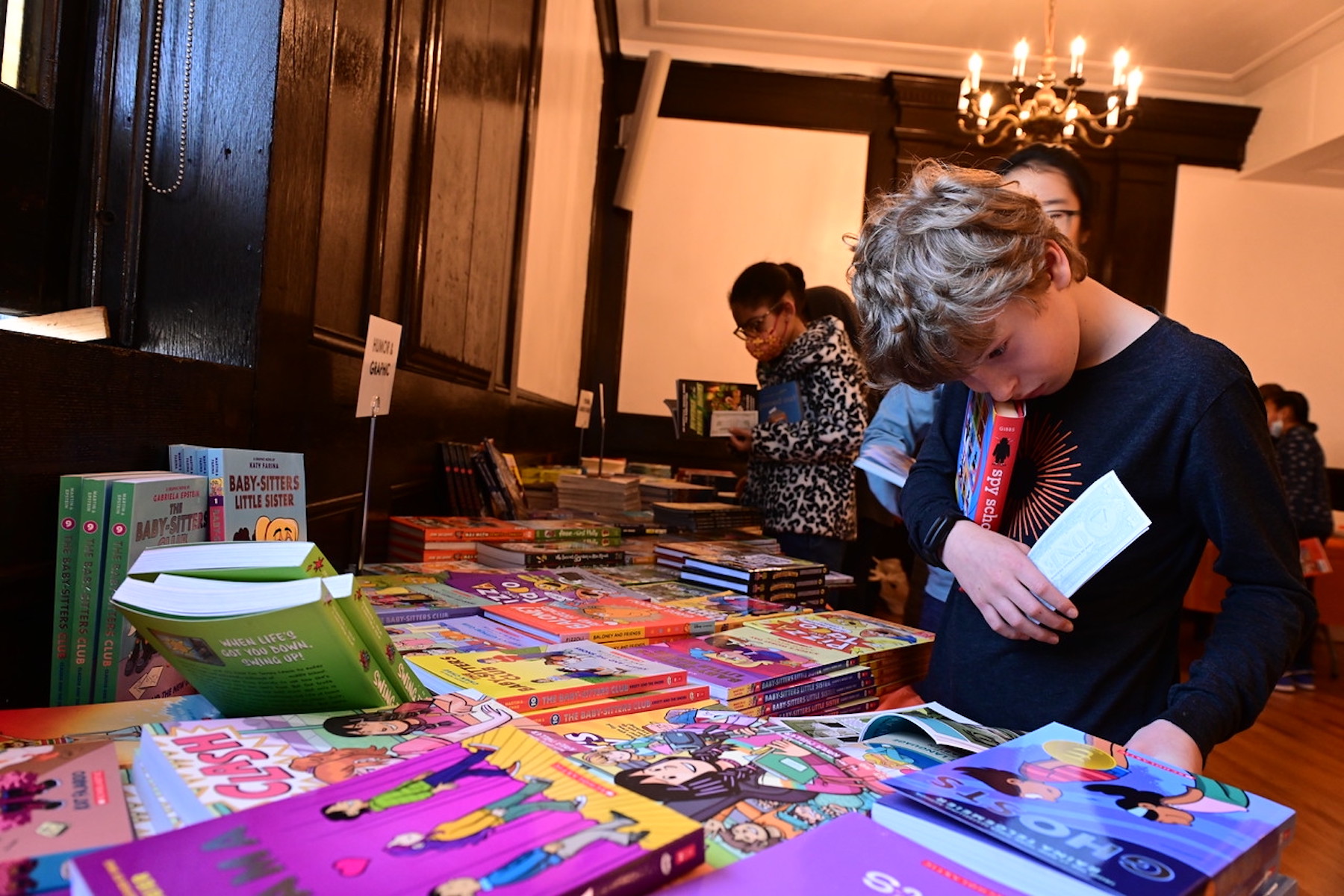 Ethical Culture student looks intently at a book while holding another in his arms at the Book Fair.