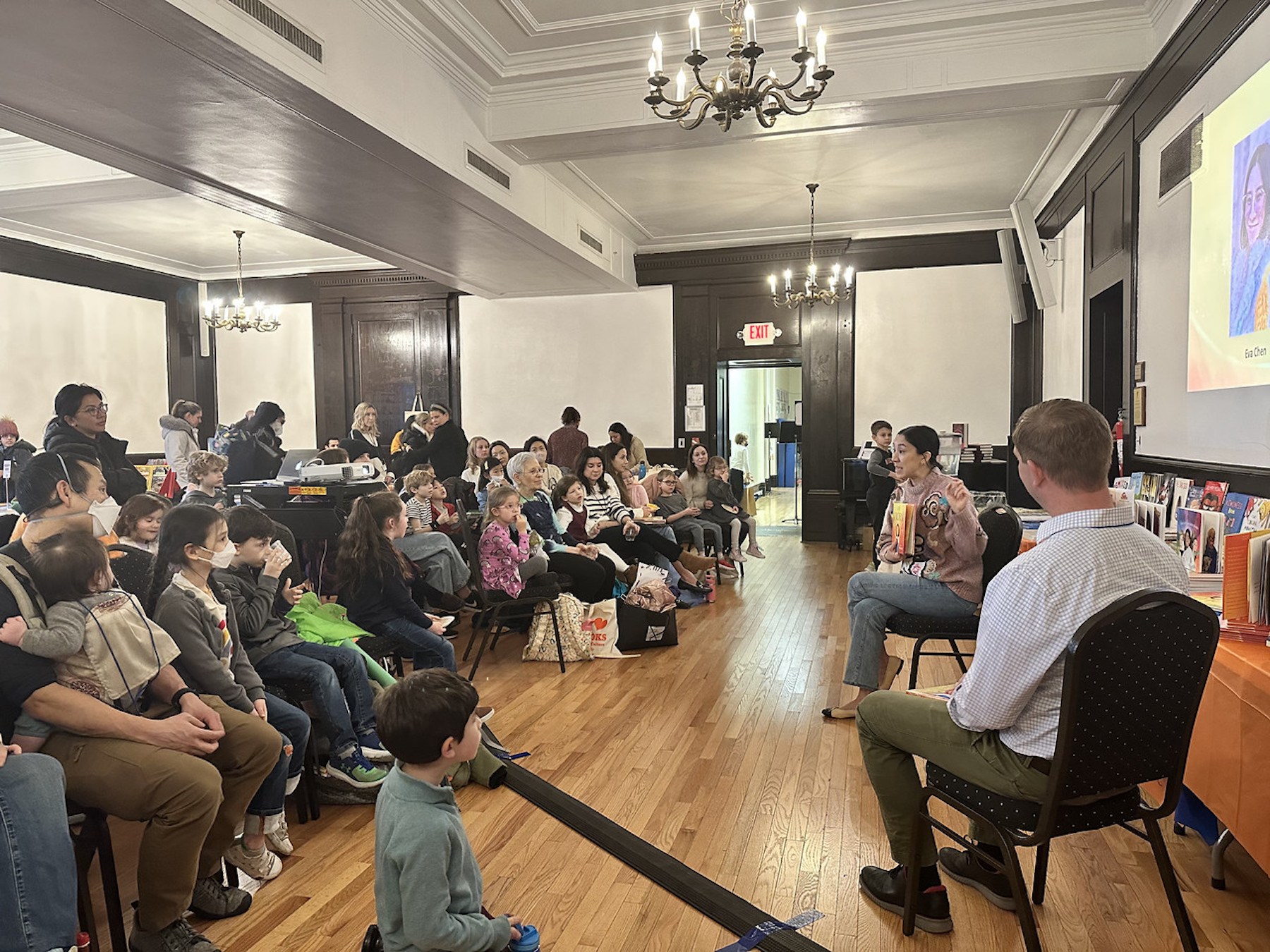 Author Eva Chen holds up book and speaks to a room full of students and parents eagerly listening along.