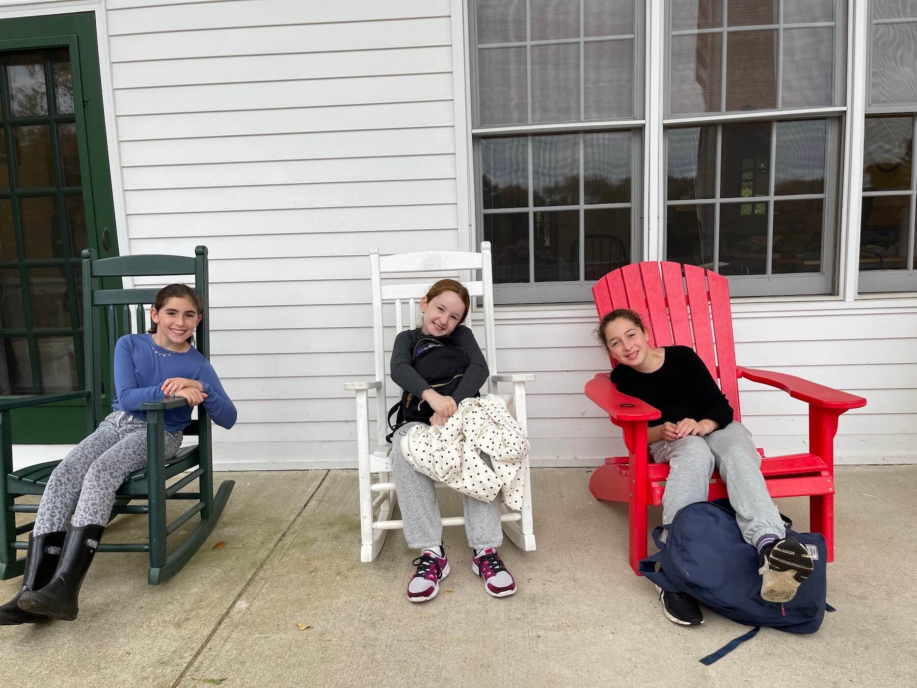 Three Ethical Culture students gather on porch, smiling from rocking chairs.