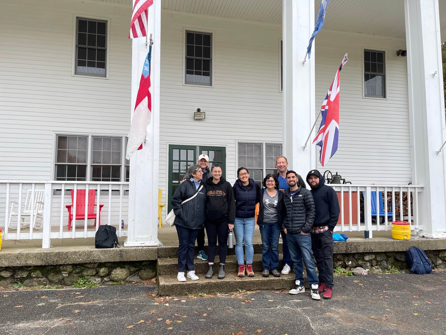 Ethical Culture faculty and staff gather on front porch of a white building between two pillars and smile.