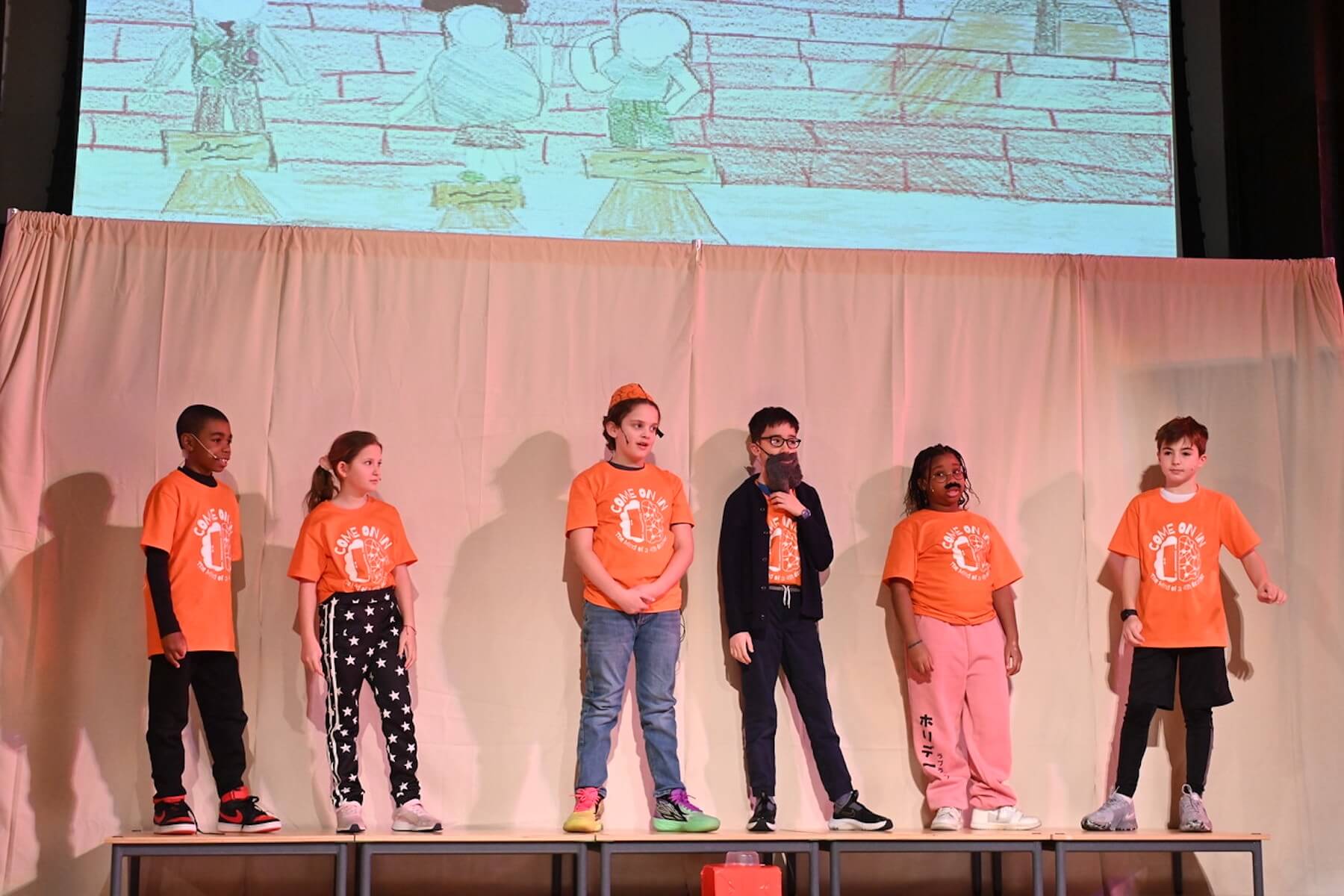 Ethical Culture students dressed in orange stand on stage during performance of 4th Grade play.