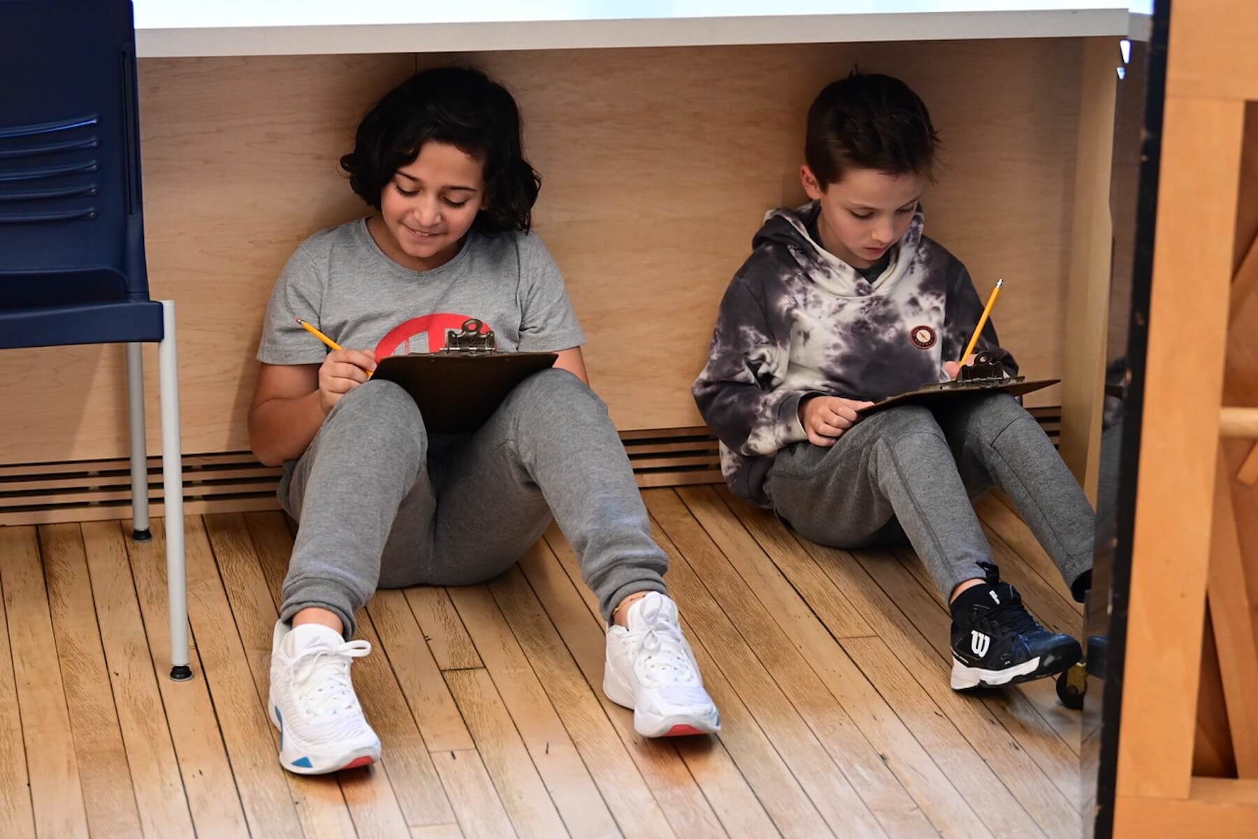 Two Ethical Culture students sit on floor in music room, drafting potential scenes for the 4th Grade play.