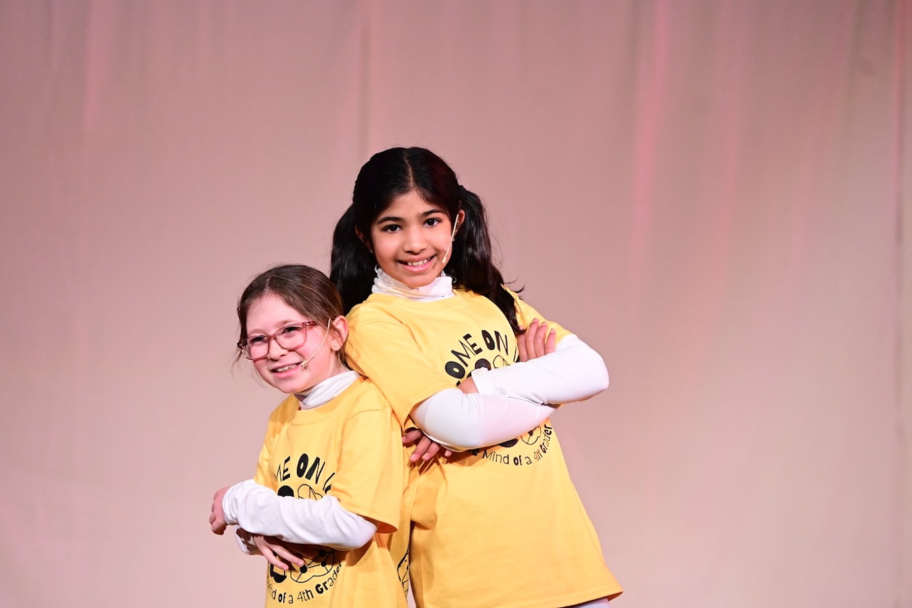 Two Ethical Culture students smile back to back on stage during performance of 4th Grade play.