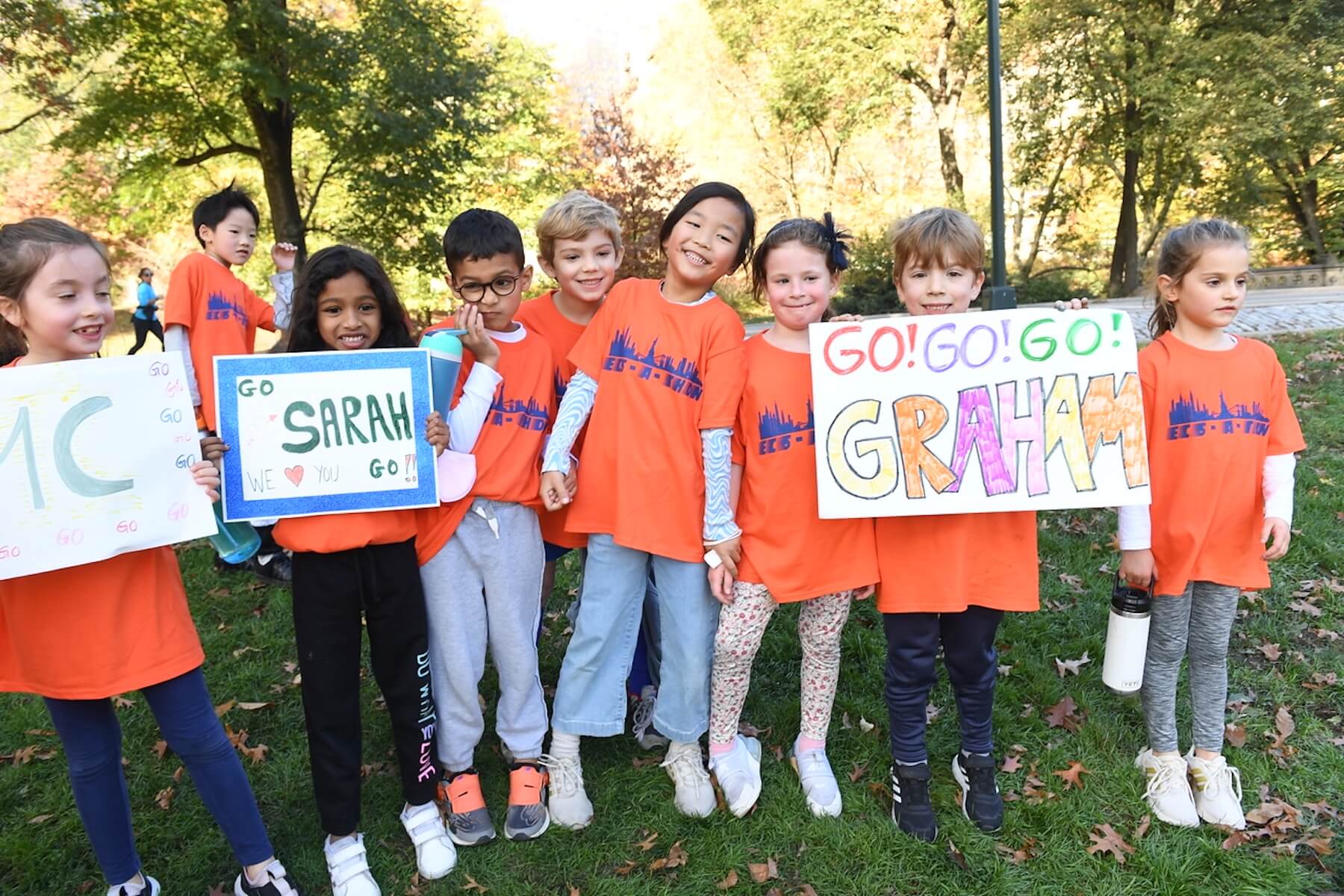 A group of ECFS students stand in grass and smile holding several signs made for them in celebration of the race.