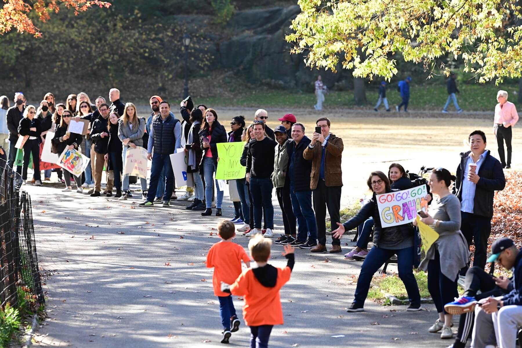 Families cheer on Ethical Culture students with signs as they run in Central Park.