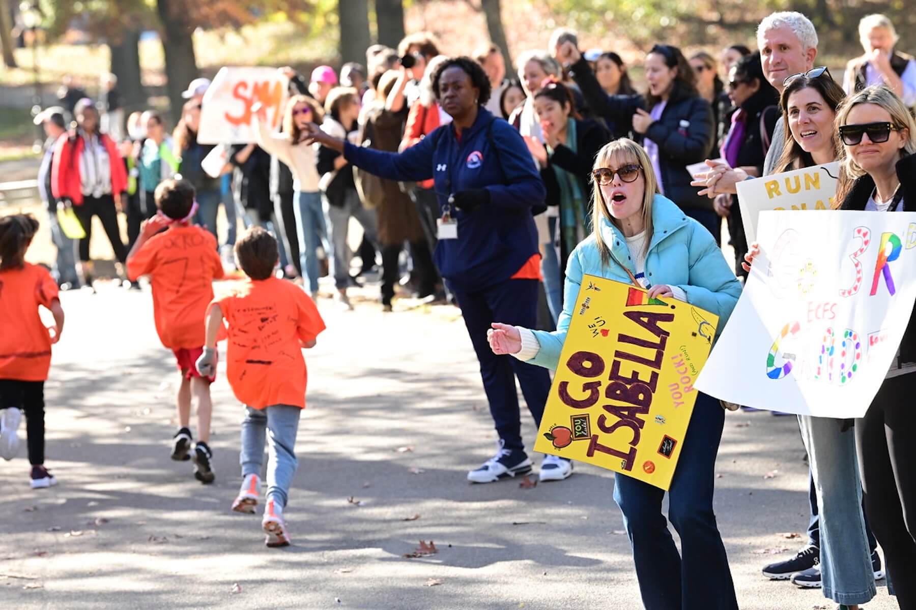 Families cheer on Ethical Culture students with signs as they run in Central Park.