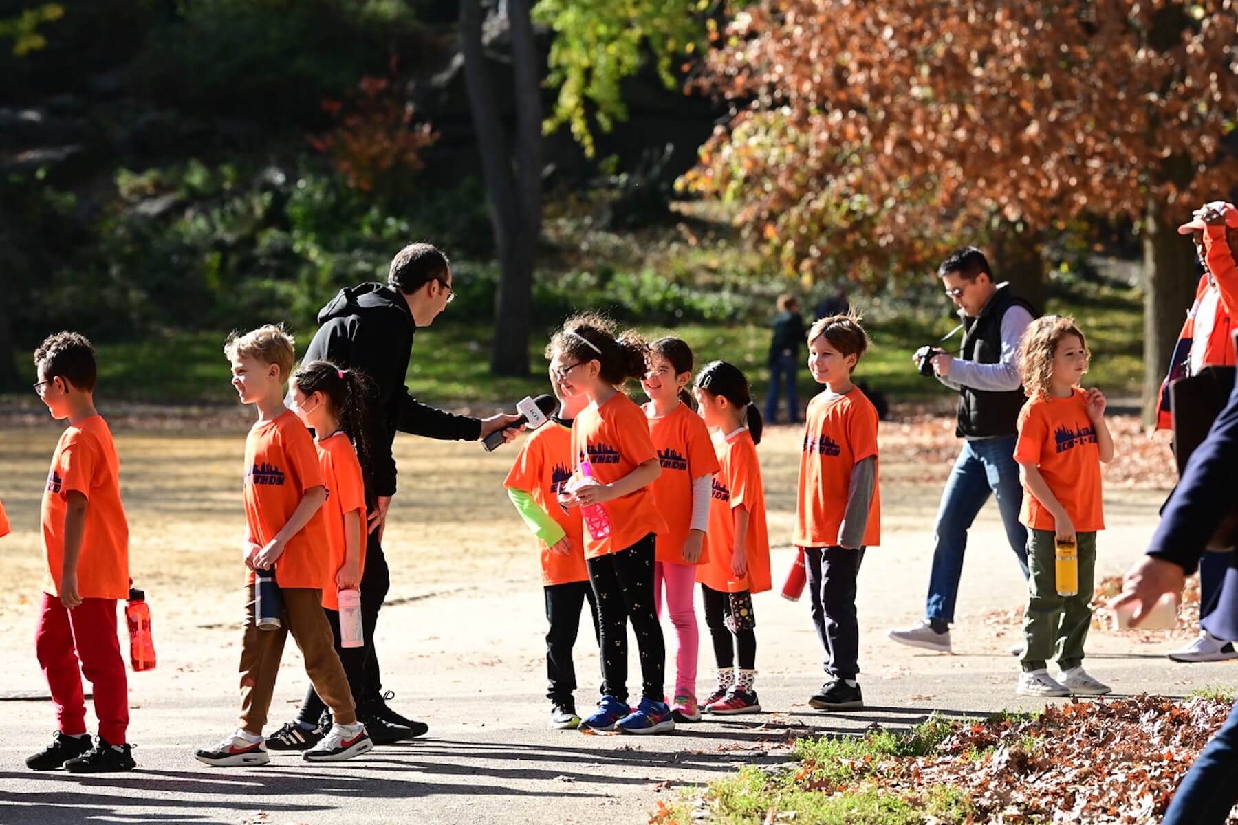 Students stand in a line, waiting to be interviewed by a man with a microphone before their race begins. One young student is speaking into the microphone.