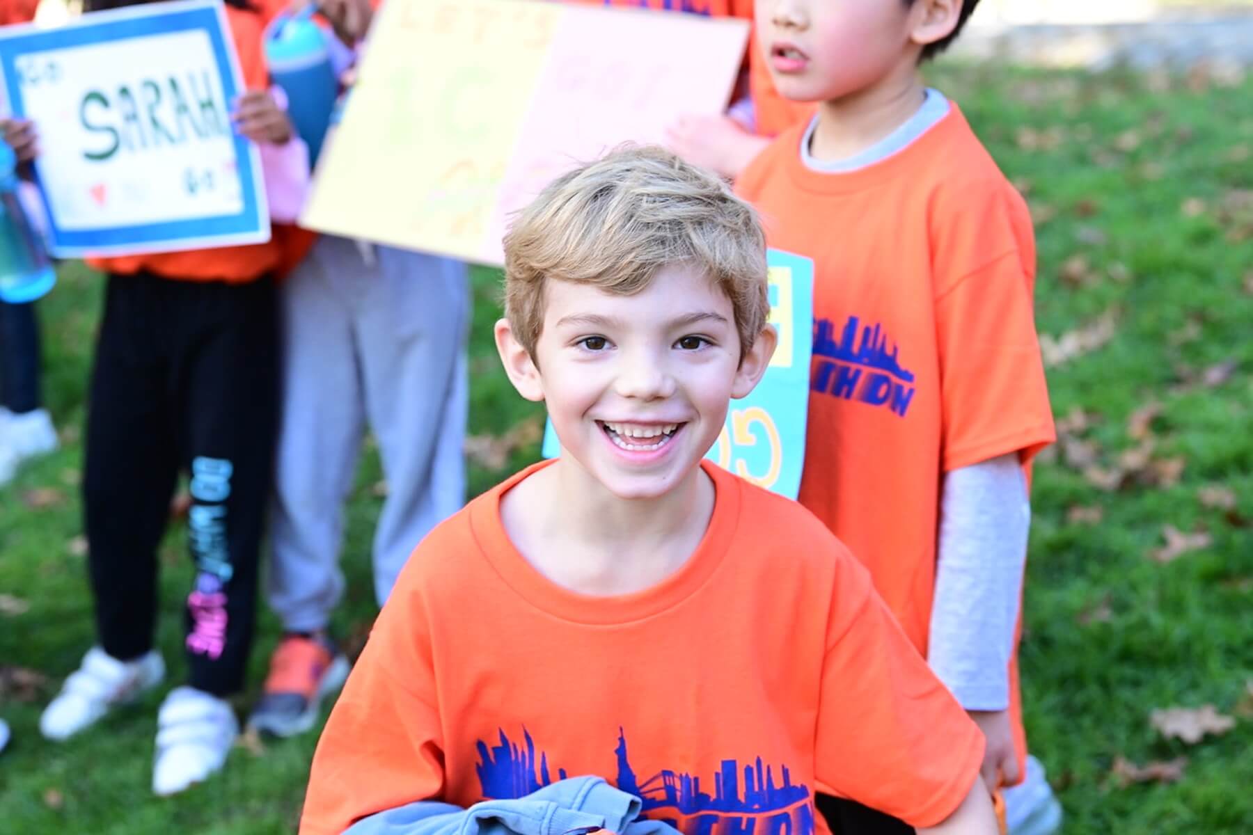 A student smiles at the camera after his race. He is holding a sweatshirt in his hand.