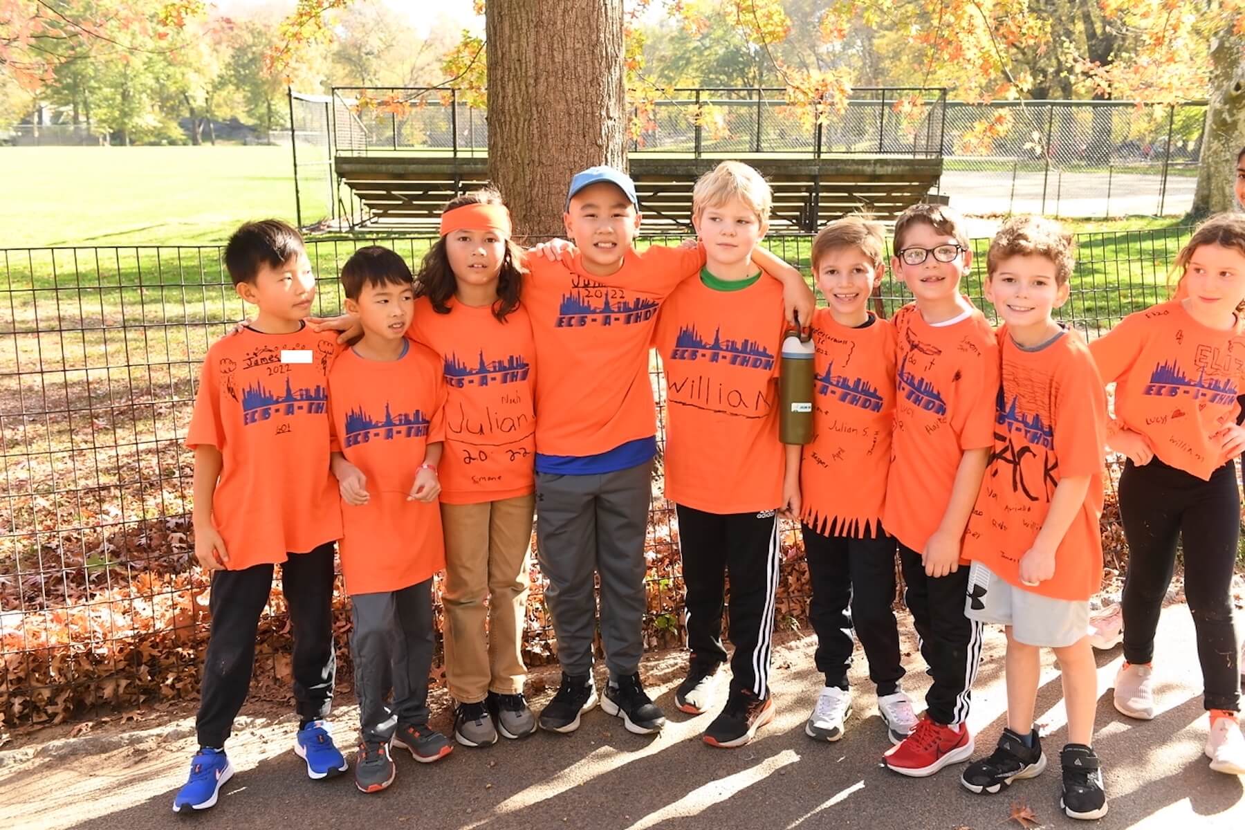 Group of students poses in front of a fence in Central Park. They are all wearing their orange ECS-a-Thon shirts.