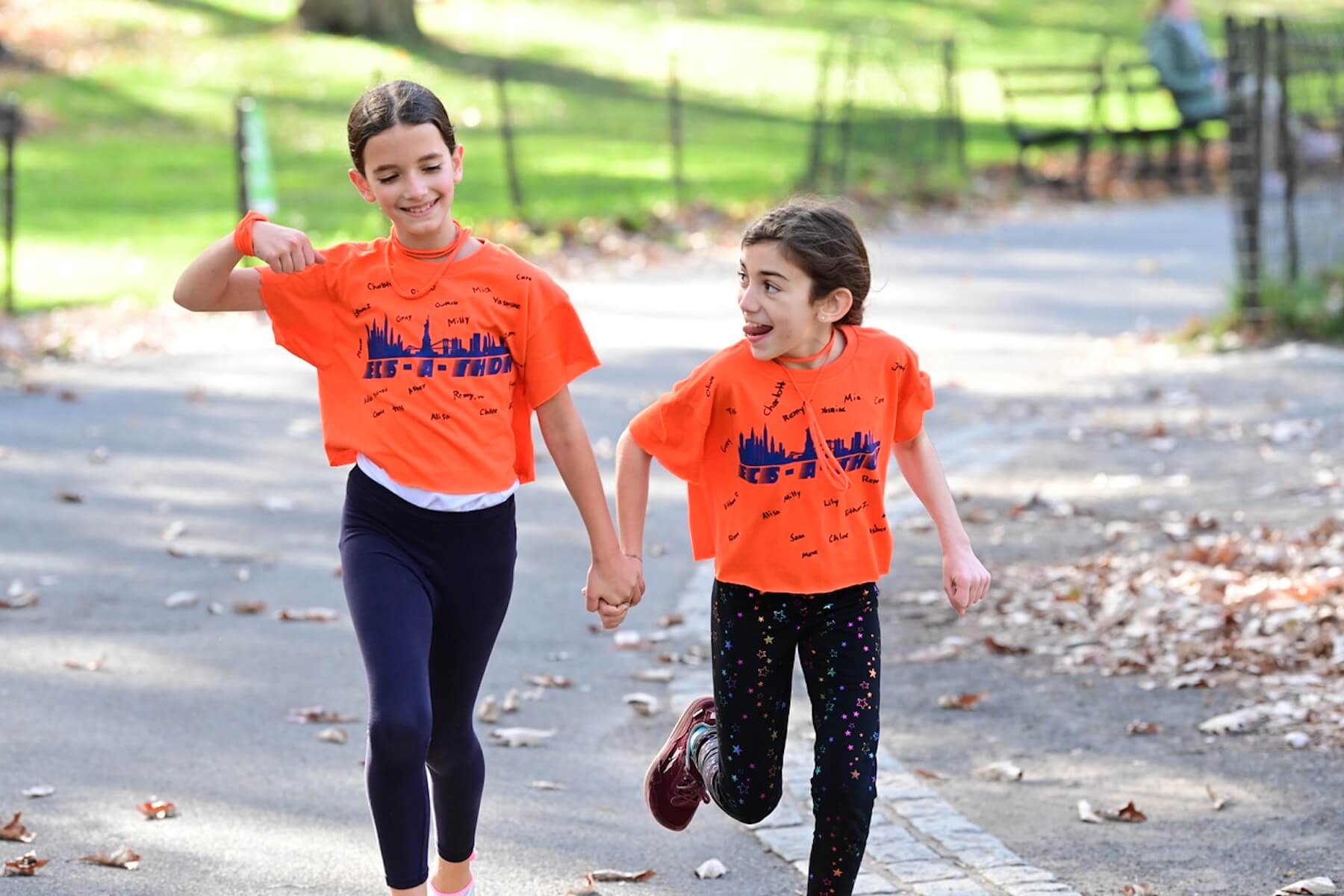 Two students run in Central Park while holding hands.