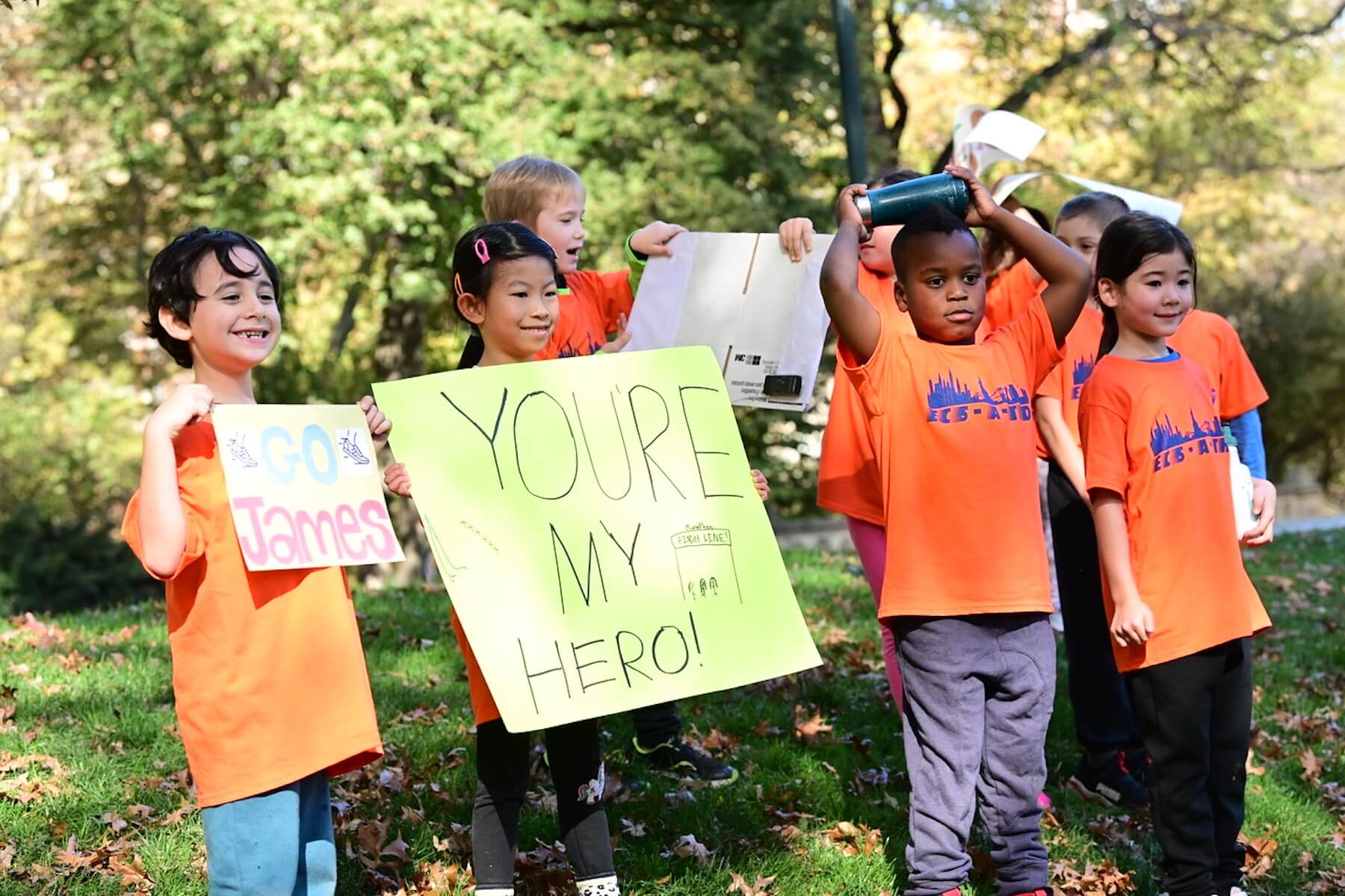 Ethical Culture students stand in the grass and hold signs while smiling. They've just completed their races.