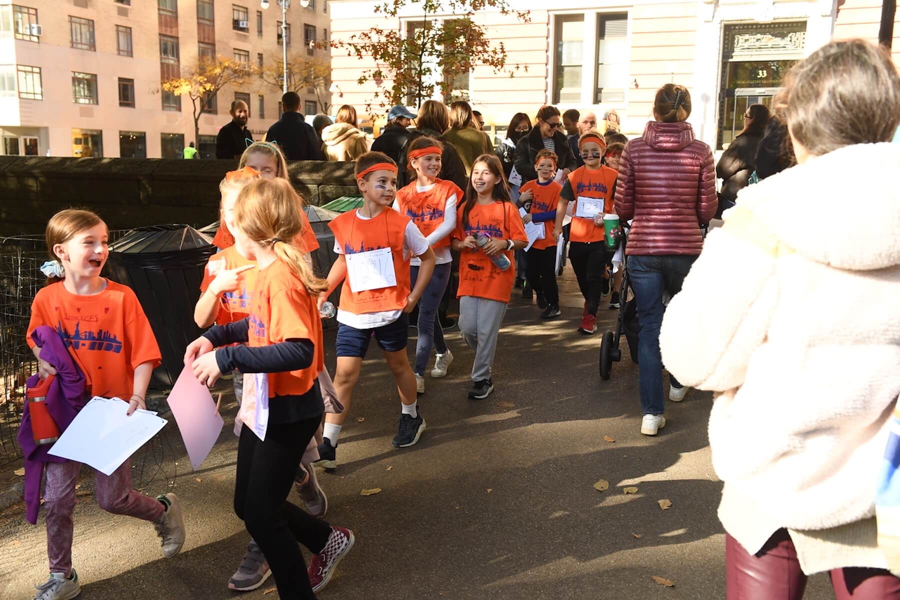 Students walk in a line into Central Park wearing orange shirts and holding signs. They are getting ready to run in Ethical Culture's annual ECS-a-Thon.