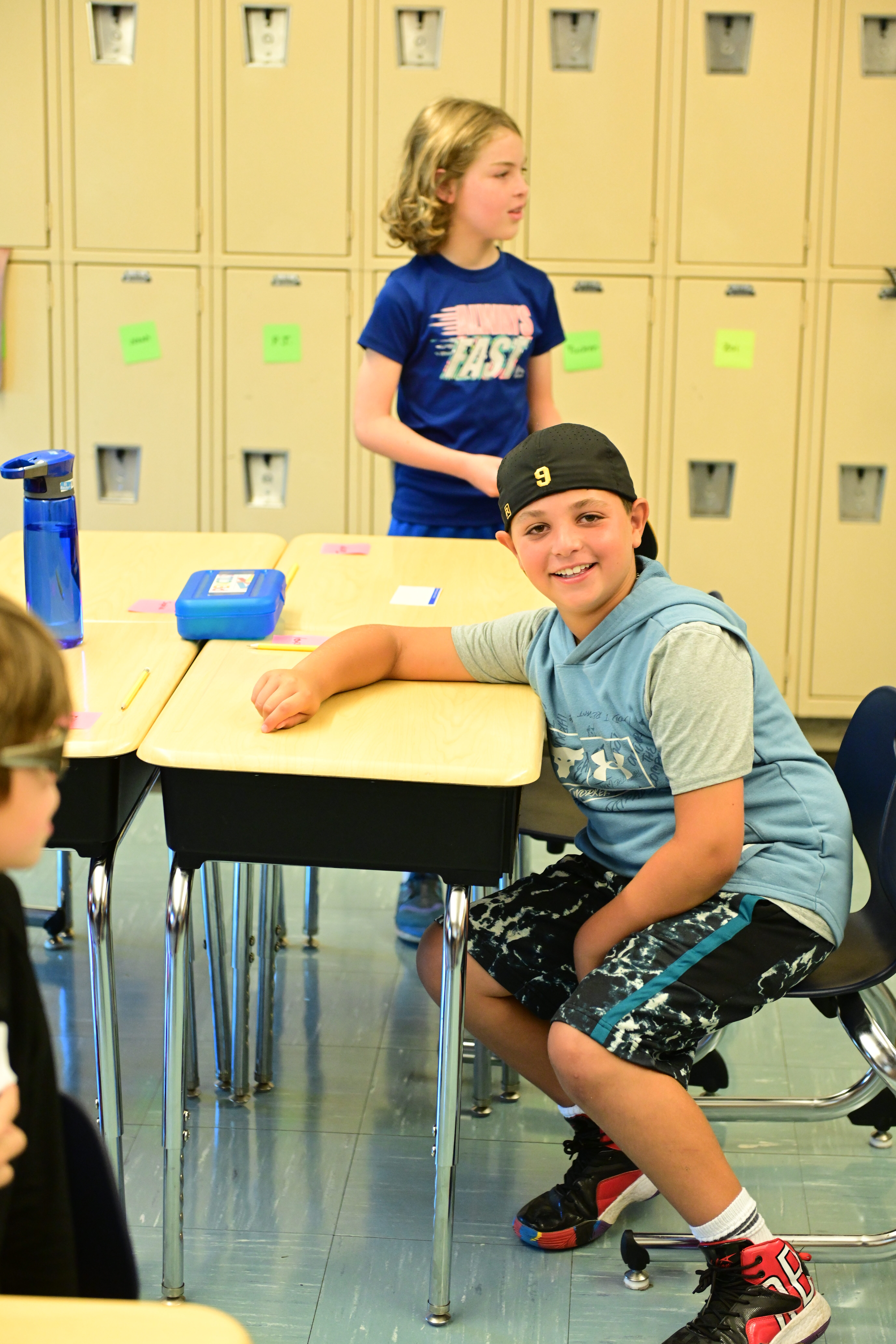 A student sits at a desk in a classroom at Fieldston Lower and smiles at the camera
