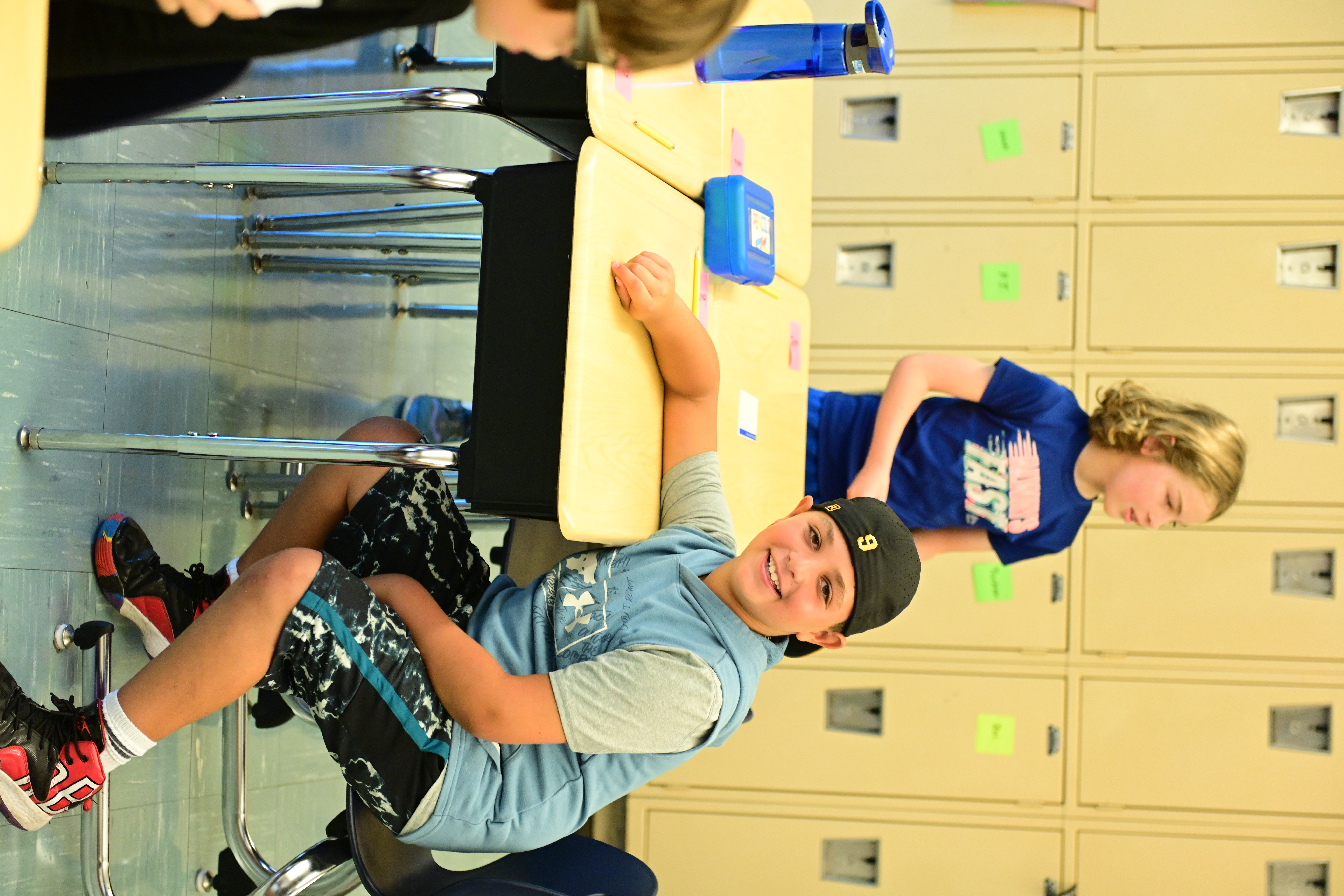 A student sits at a desk in a classroom at Fieldston Lower and smiles at the camera