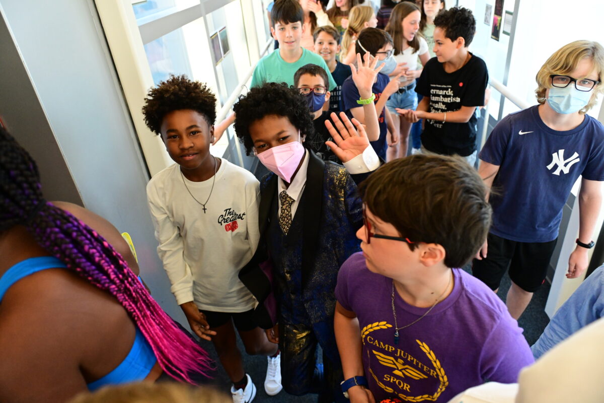 Students at Fieldston Middle wave at the camera as they walk down a hallway