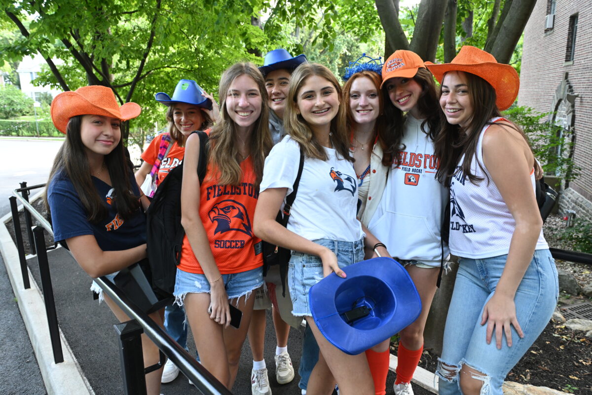 A group of Fieldston Upper students pose for the camera wearing ECFS gear and orange and blue hats