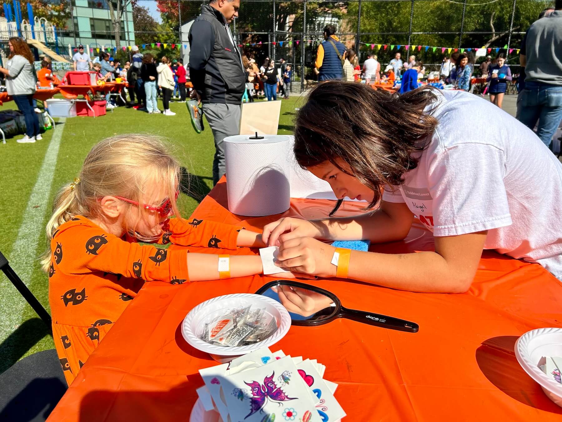 Ethical Culture Fieldston School Fieldston Lower student places temporary tattoo on a younger student during carnival