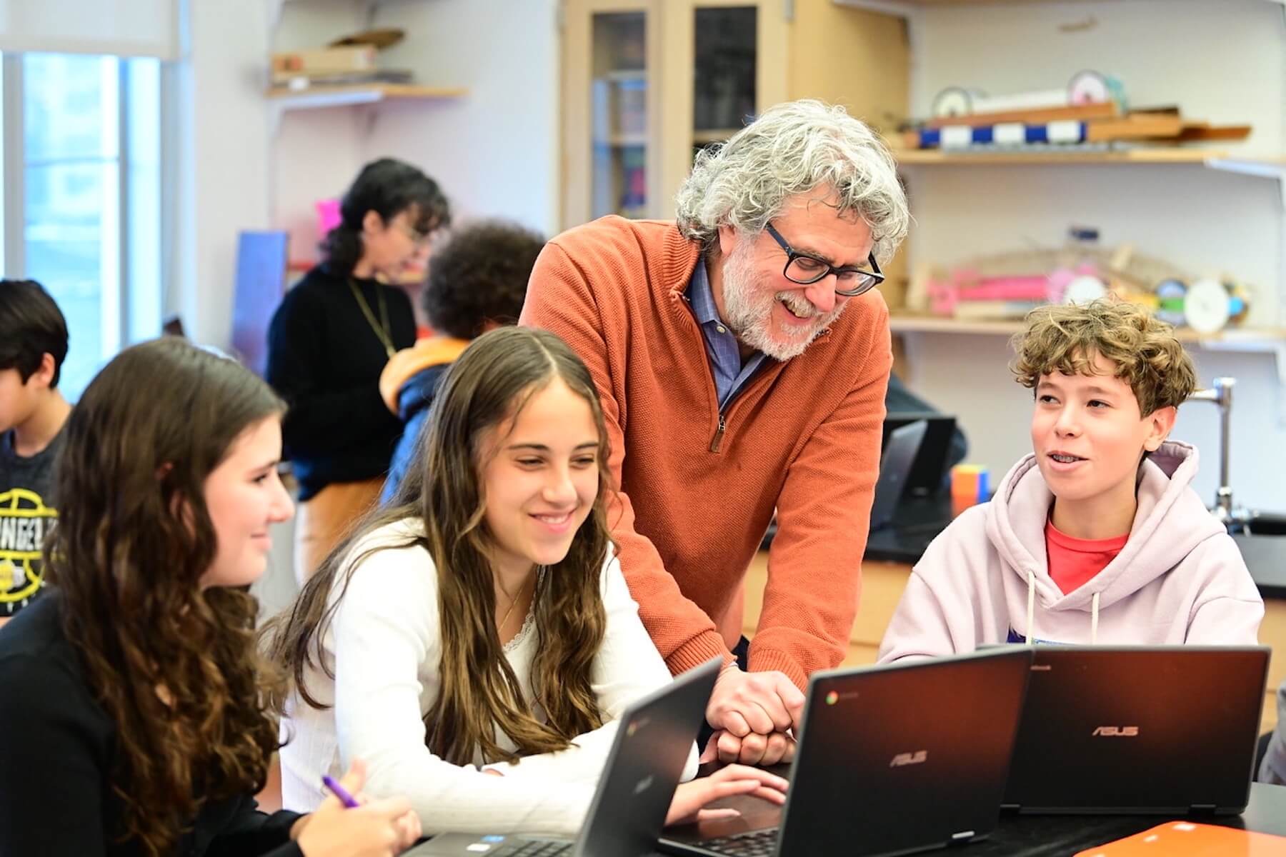 Joe Algrant at Ethical Culture Fieldston School stands over smiling at three students in Middle School