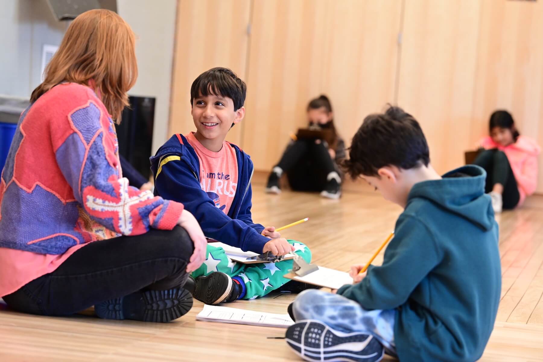 An Ethical Culture Fieldston School student sits on floor with work smiling at teacher from Ethical Culture