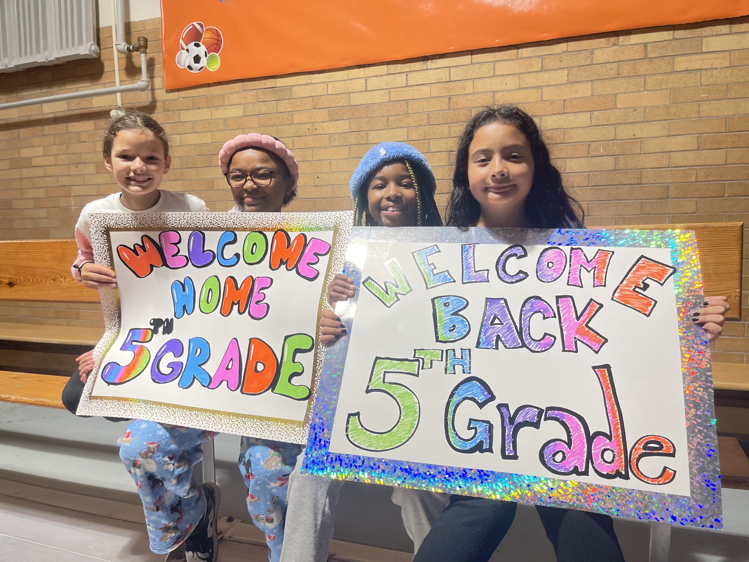Students hold signs welcoming back 5th Graders after their trip.