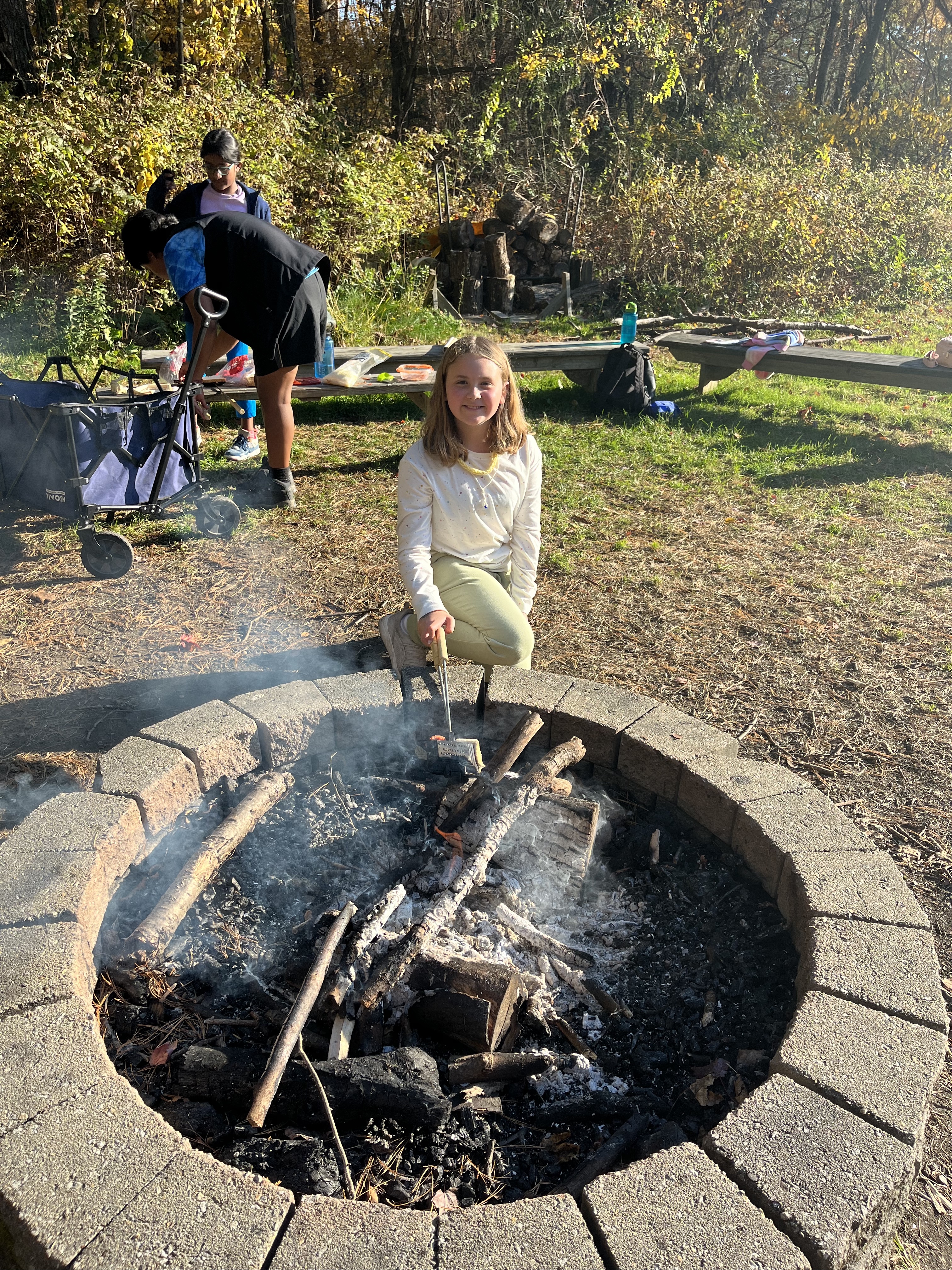 Student poses in front of firepit while making s'mores.
