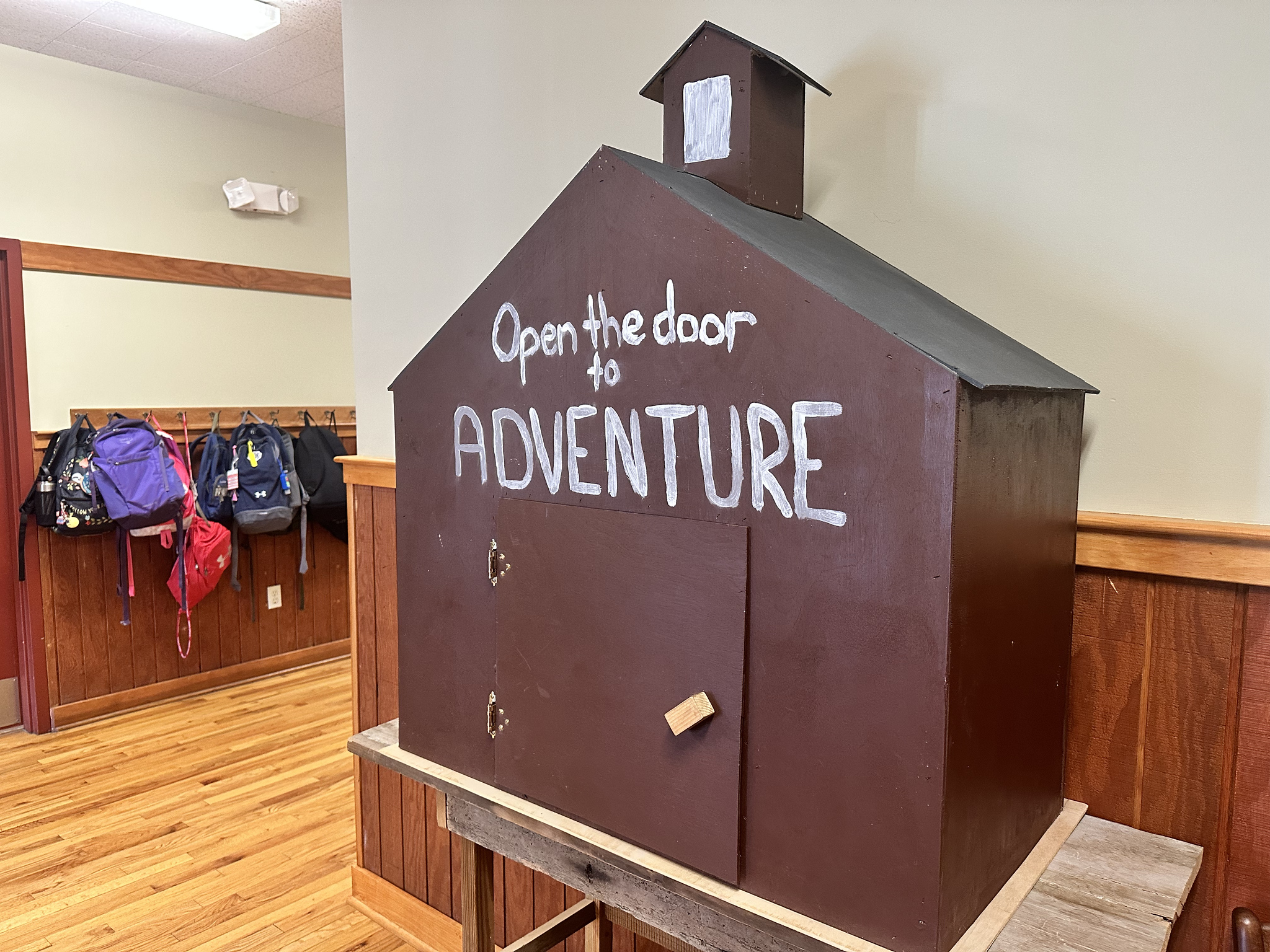 Photo of mini wooden schoolhouse at Nature's Classroom that says "Open the Door to Adventure."